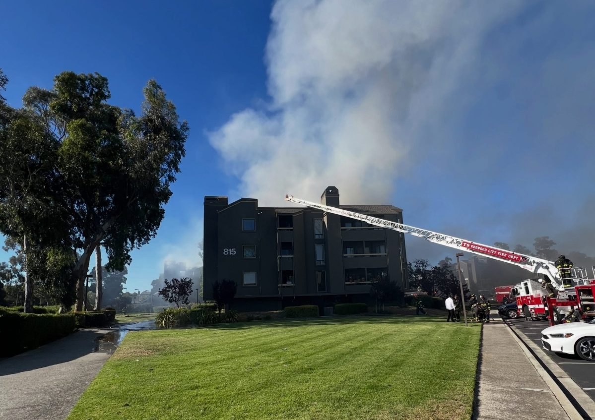 Aerial ladder truck sprays water on a smoke-filled multi-story apartment building.