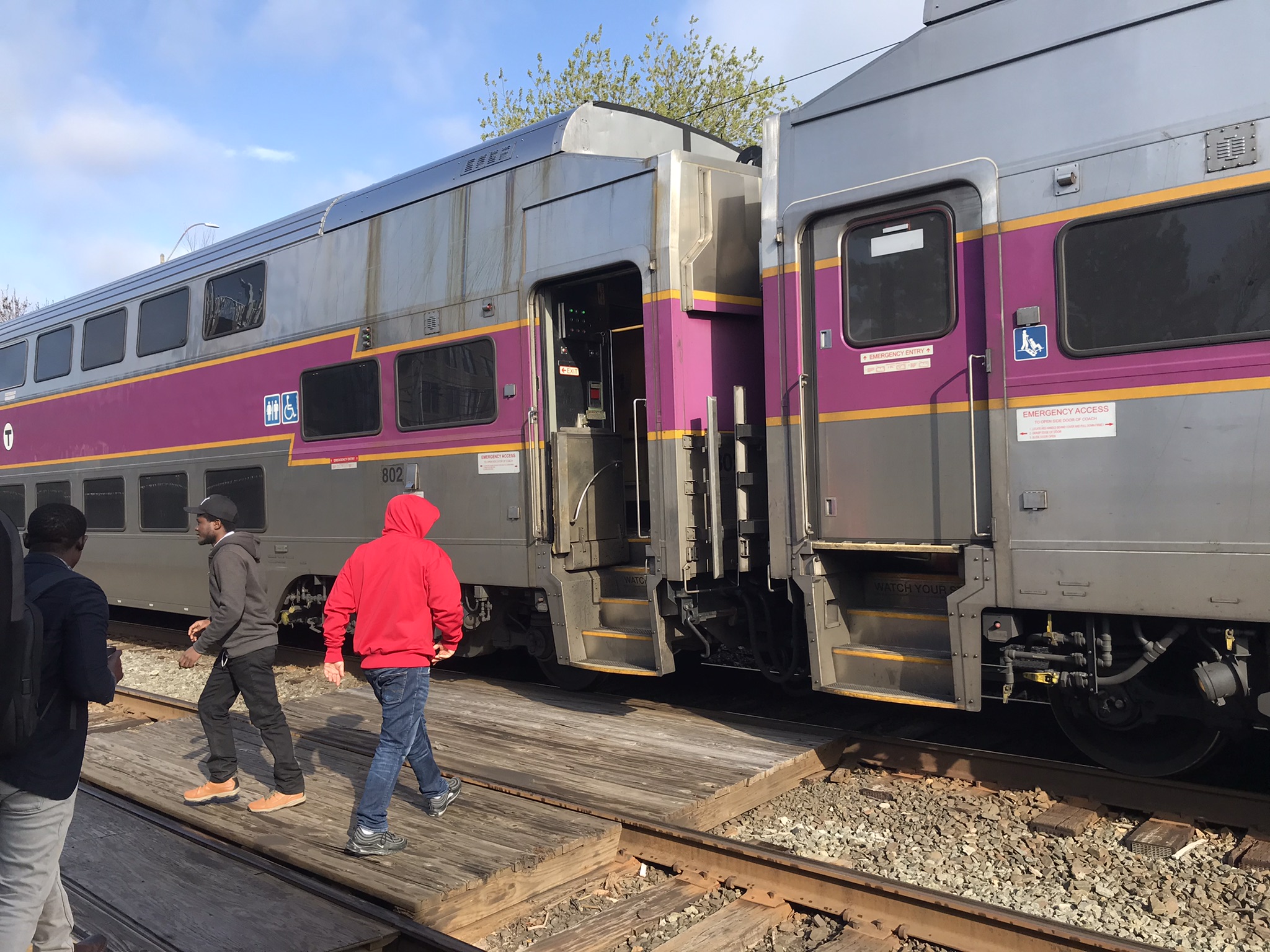 Passengers walk along a wooden boardwalk to board a double-decker commuter rail train at a station platform.