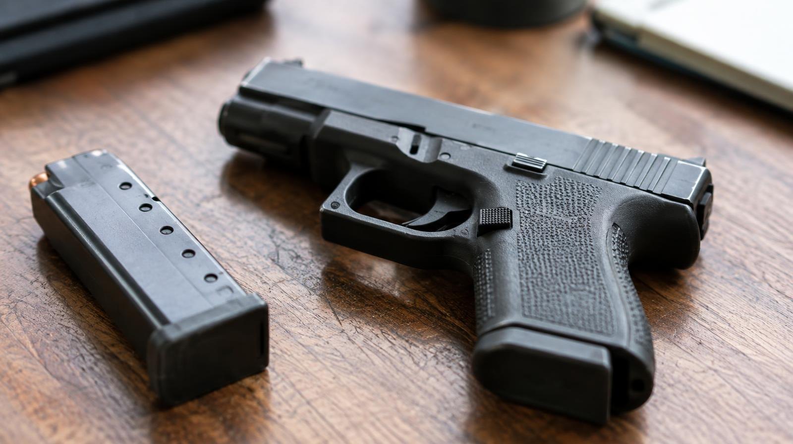 A black semi-automatic pistol resting on a wooden surface beside a detached magazine.