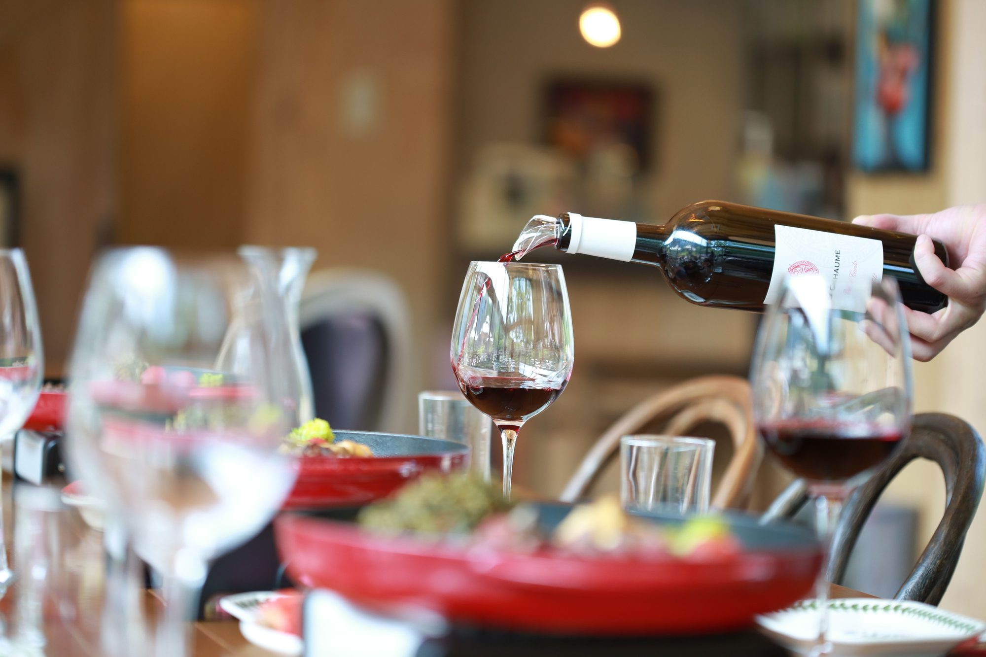 Close-up of red wine being poured into a glass during an elegant dinner setting with blurred background.