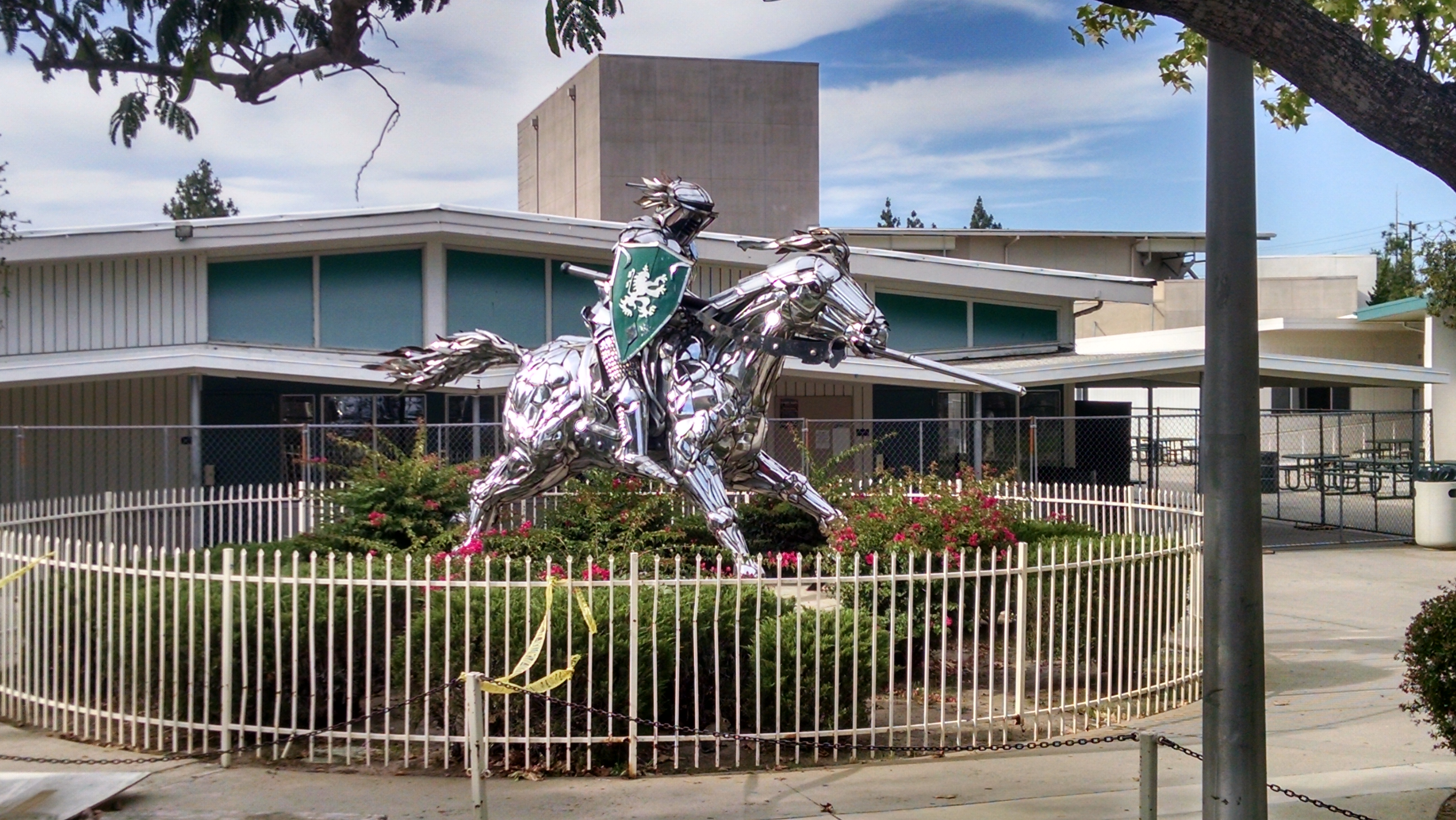 Chrome knight-on-horseback sculpture in front of a school building.