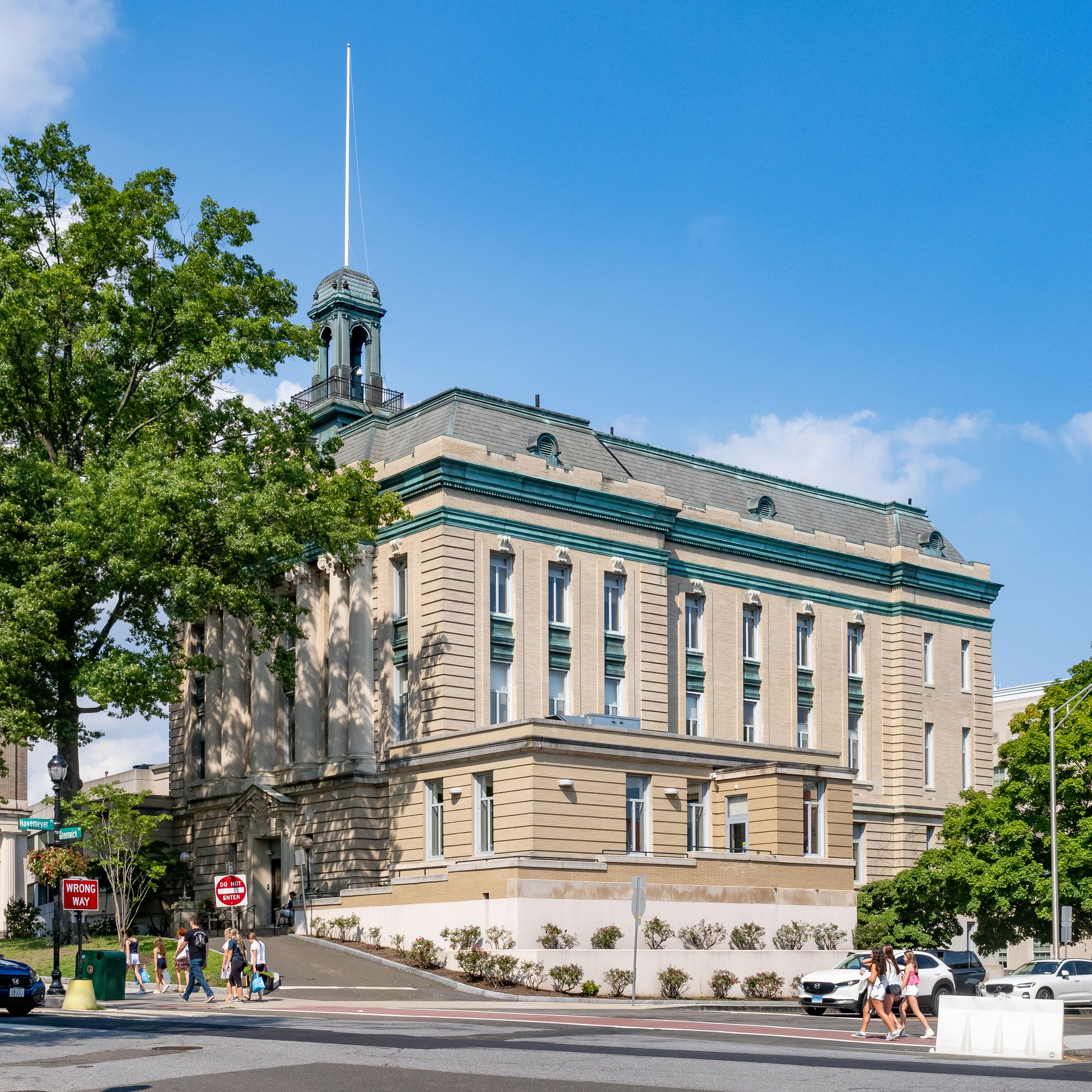 Multi-story neoclassical building with cupola and flagpole on a sunny street corner.
