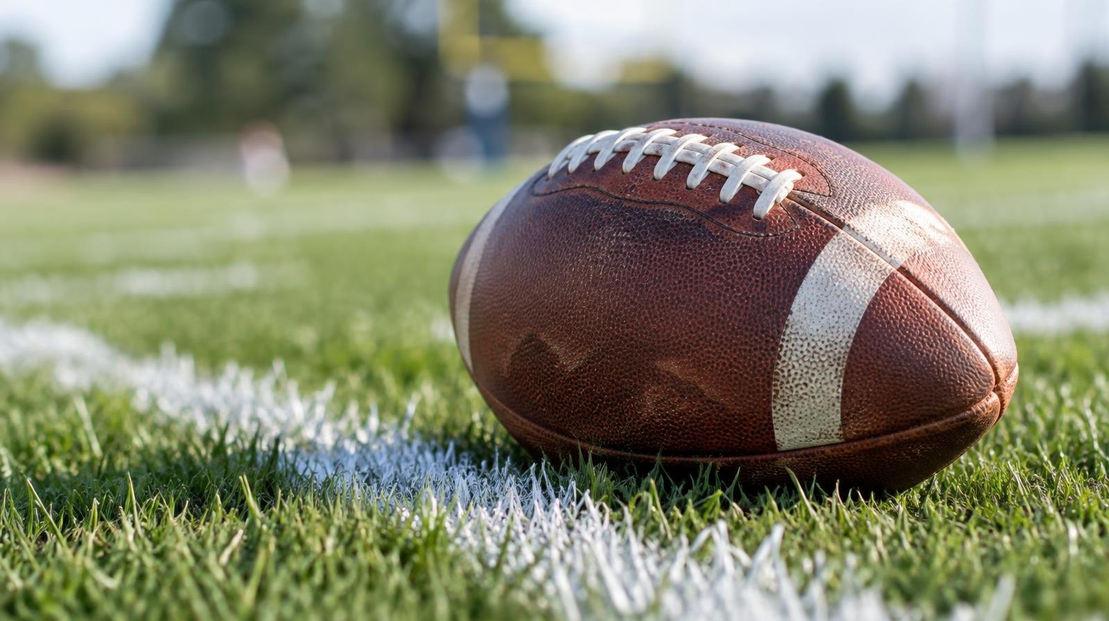 An American football resting on green grass beside a white painted yard line.