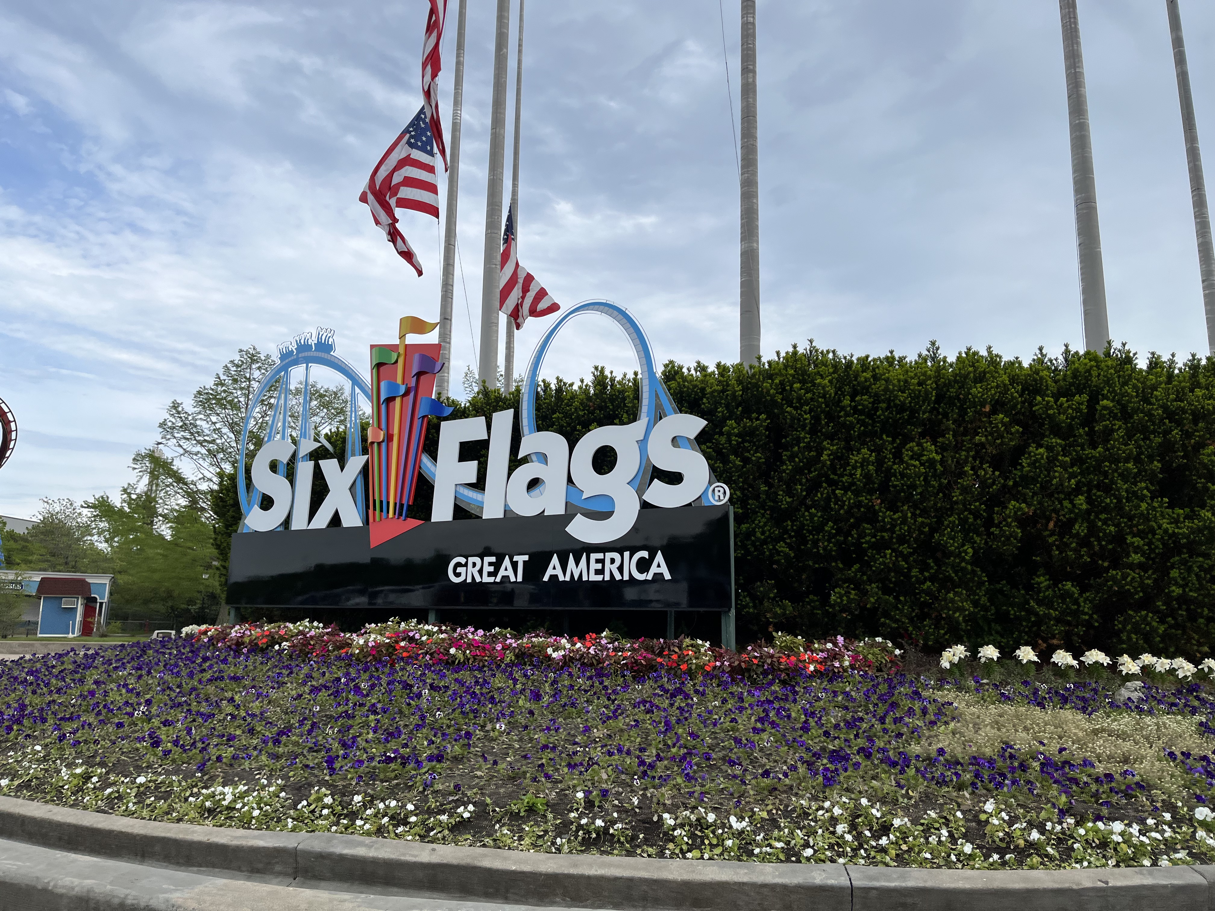 Colorful Six Flags entrance sign surrounded by flower beds and tall flagpoles.