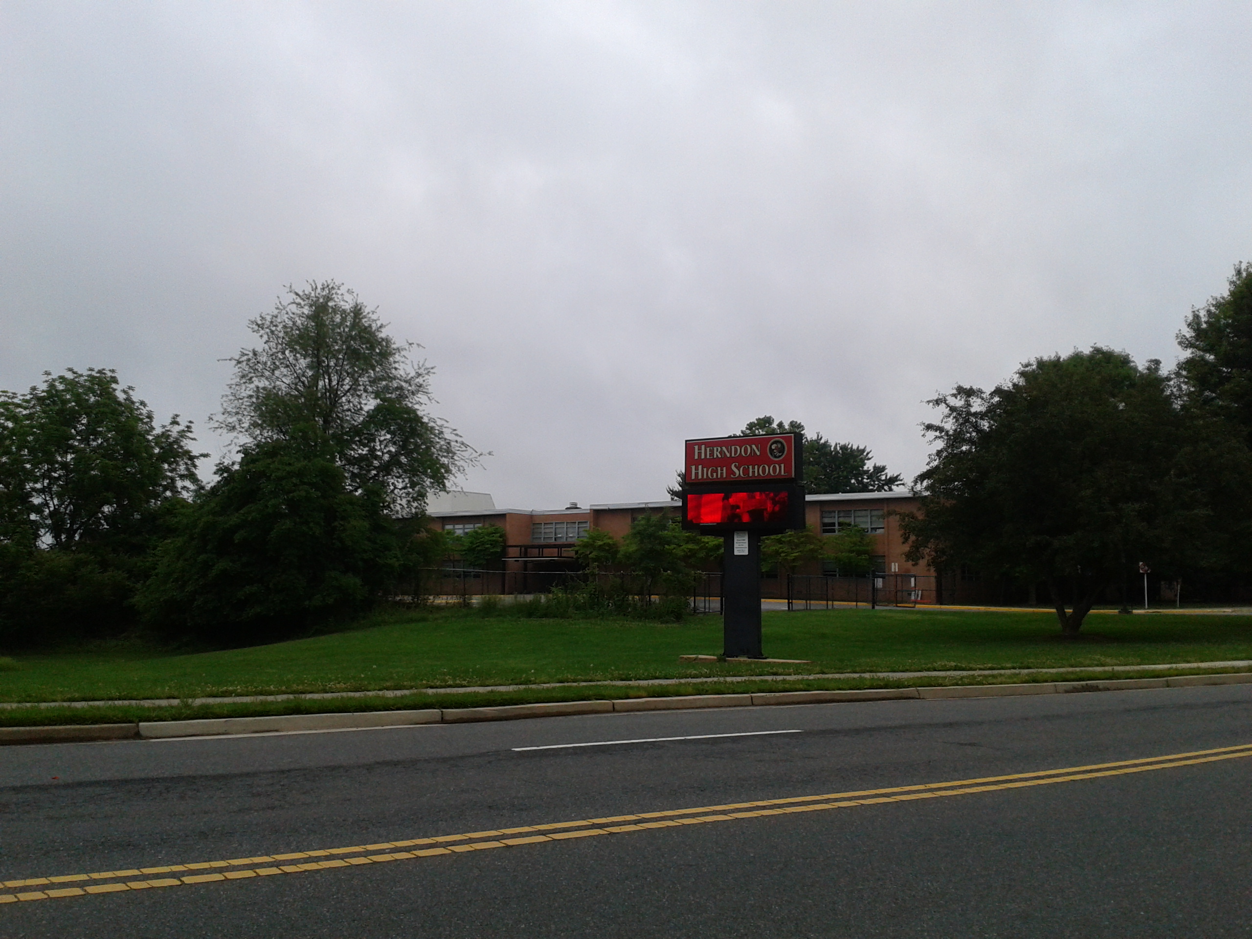 Brick school building with a red electronic marquee sign on a grassy hill.