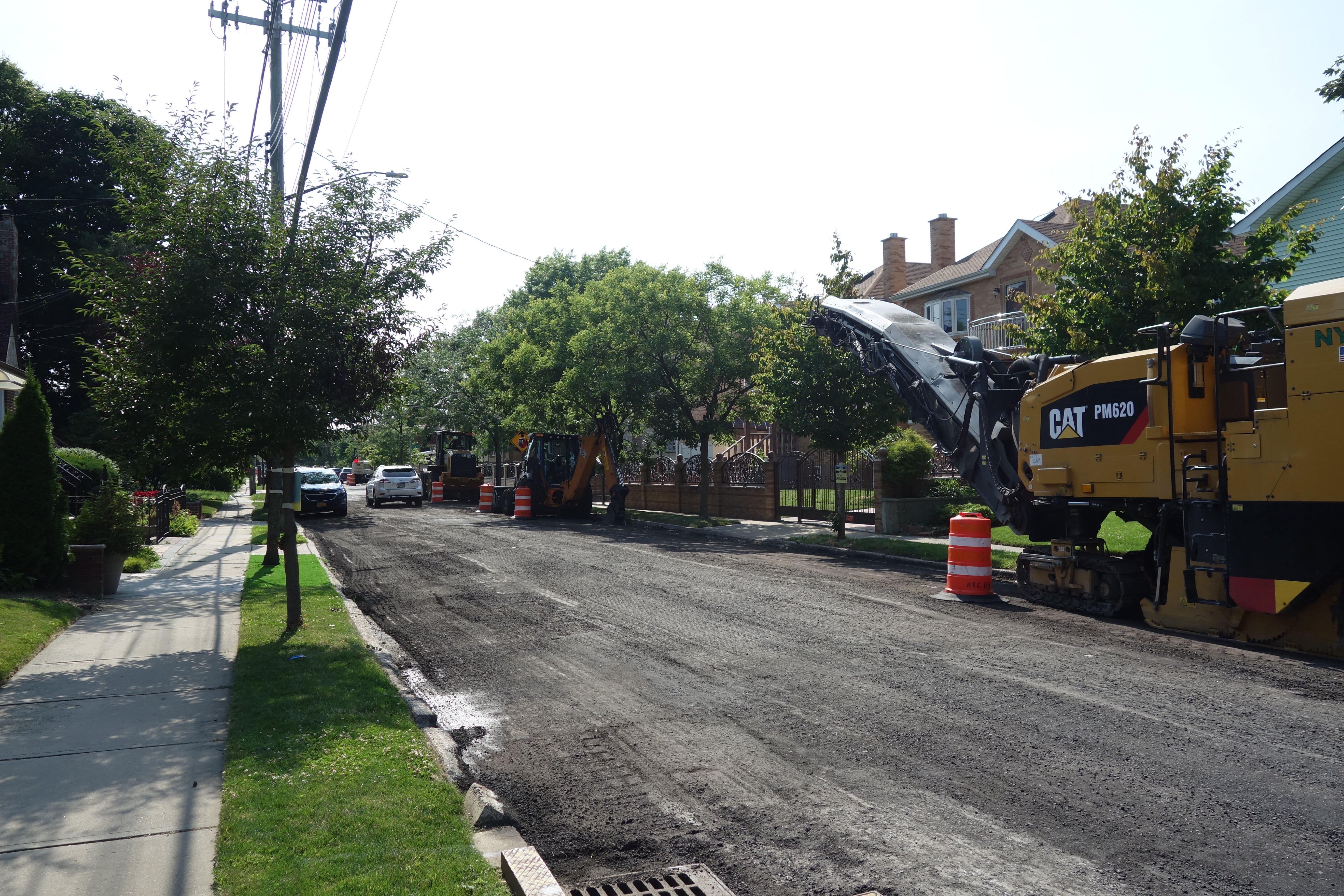 Yellow CAT milling machine on a residential street with orange traffic barrels.