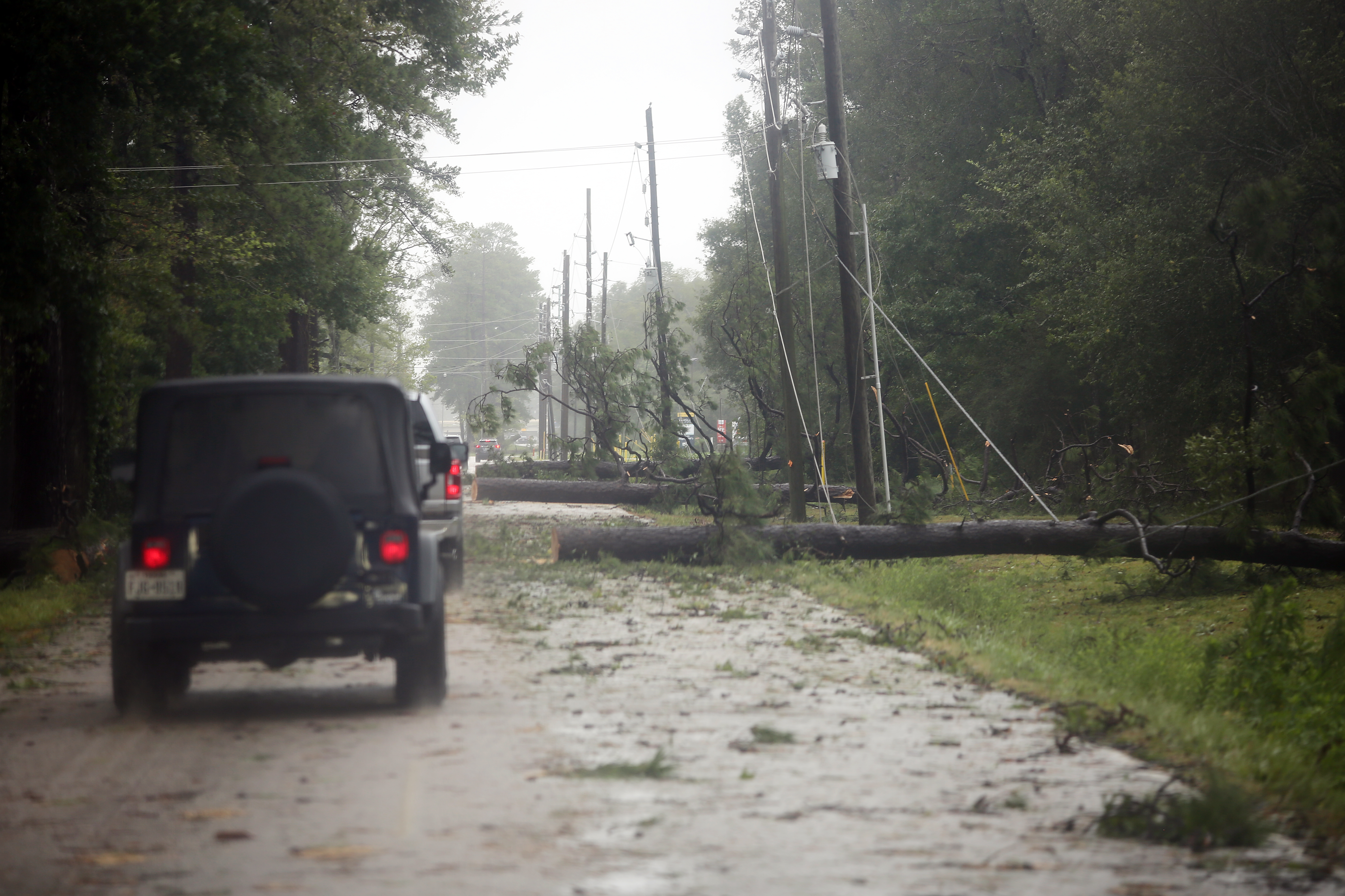 A vehicle blocked by fallen trees and downed power lines on a flooded road after a hurricane.
