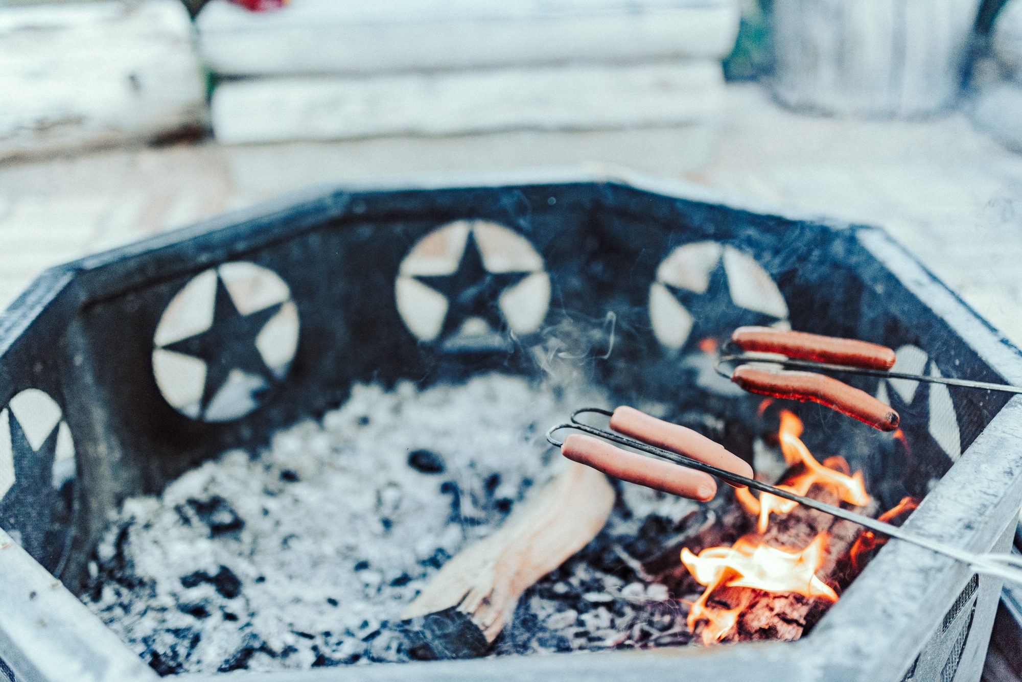 Hot dogs roasting over a rustic outdoor fire pit, perfect for a summer barbecue.