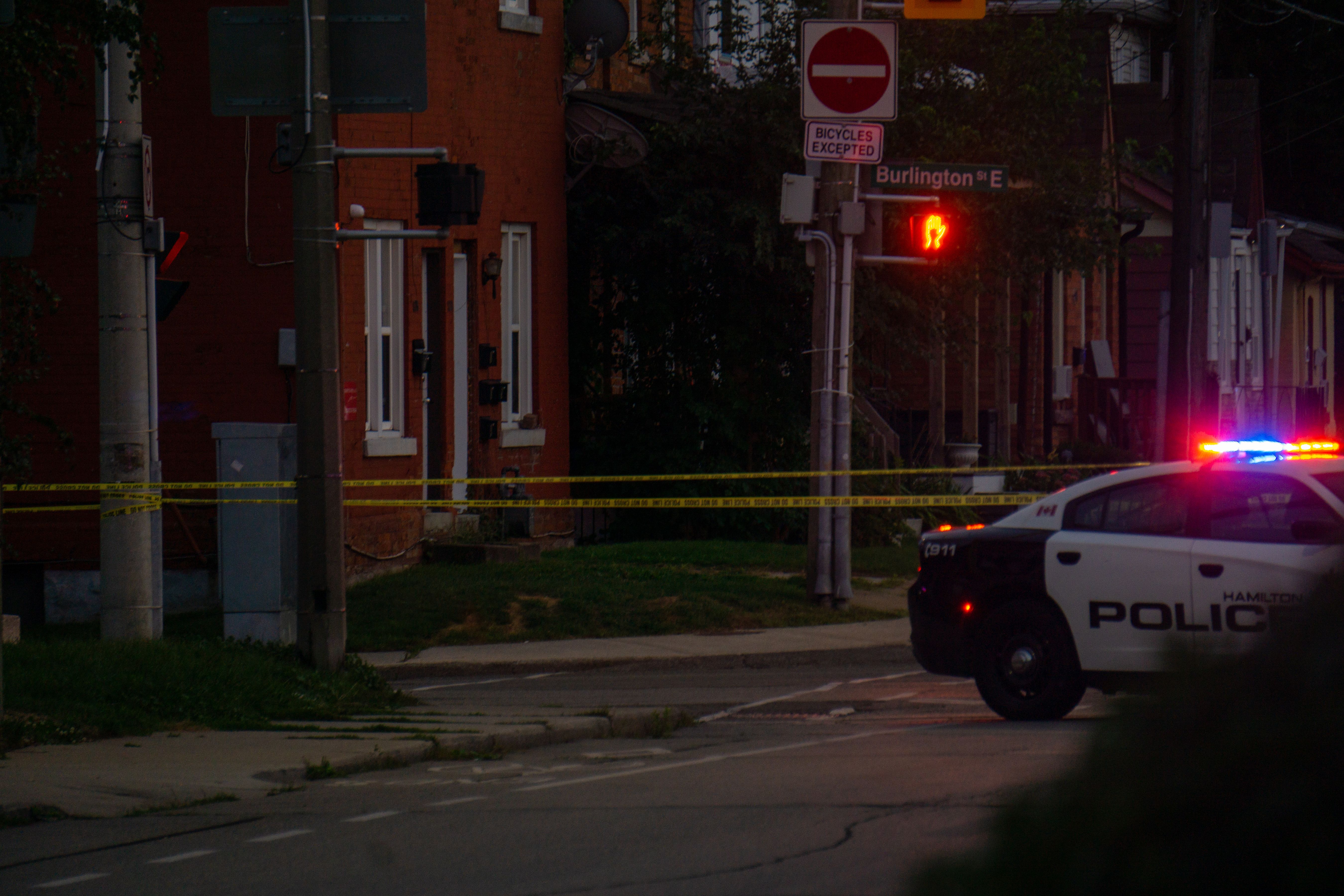 Police cruiser with flashing lights parked behind yellow crime scene tape at night.