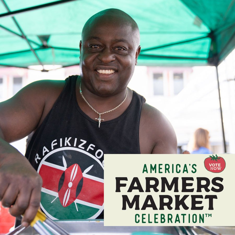 Smiling vendor at a market booth under a green canopy with a Vote Now badge overlay.