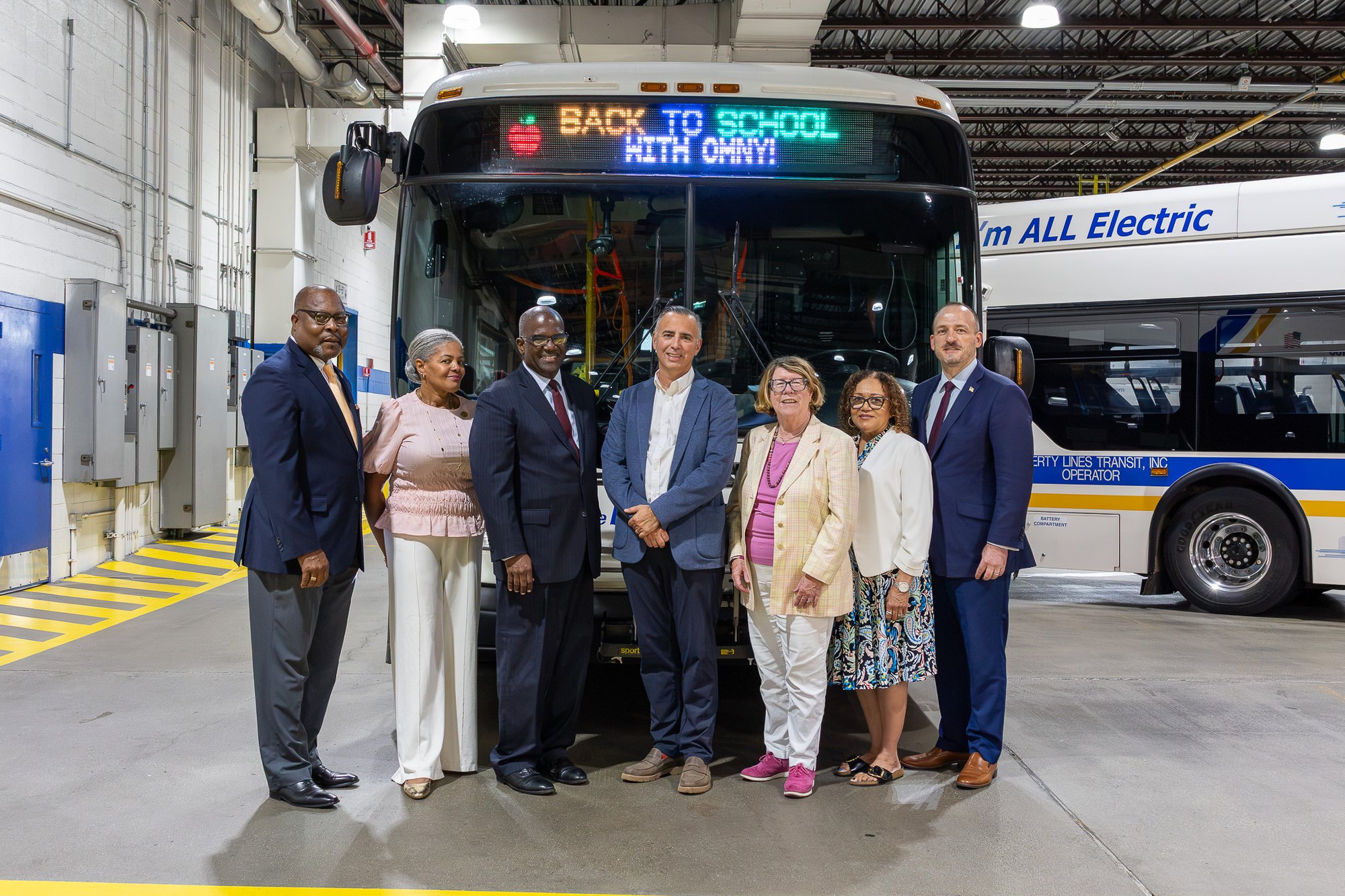Group of officials standing in front of a Bee-Line bus with a Back to School with OMNY destination sign.
