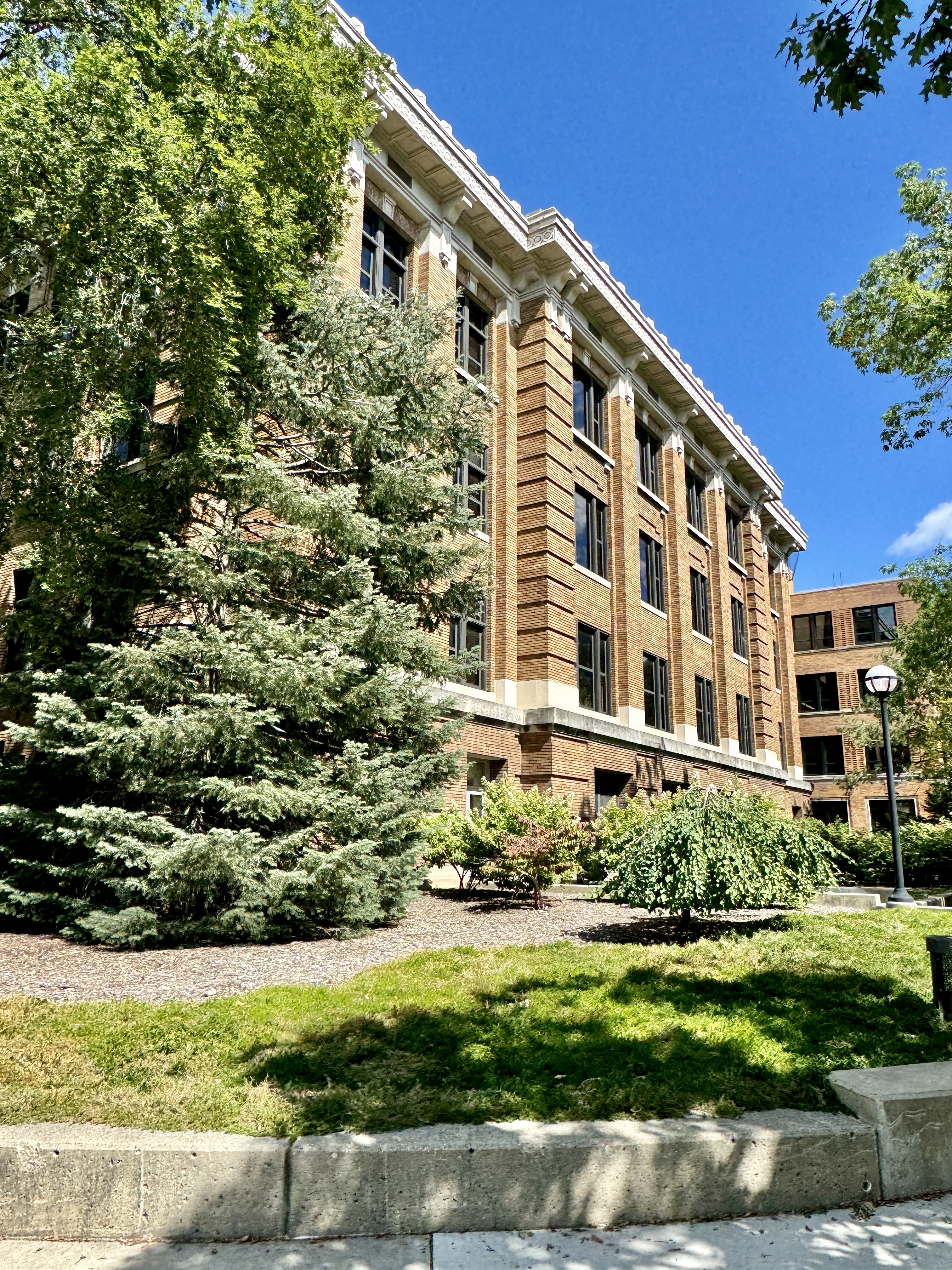 A large brick academic building on a tree-lined university campus on a sunny day.