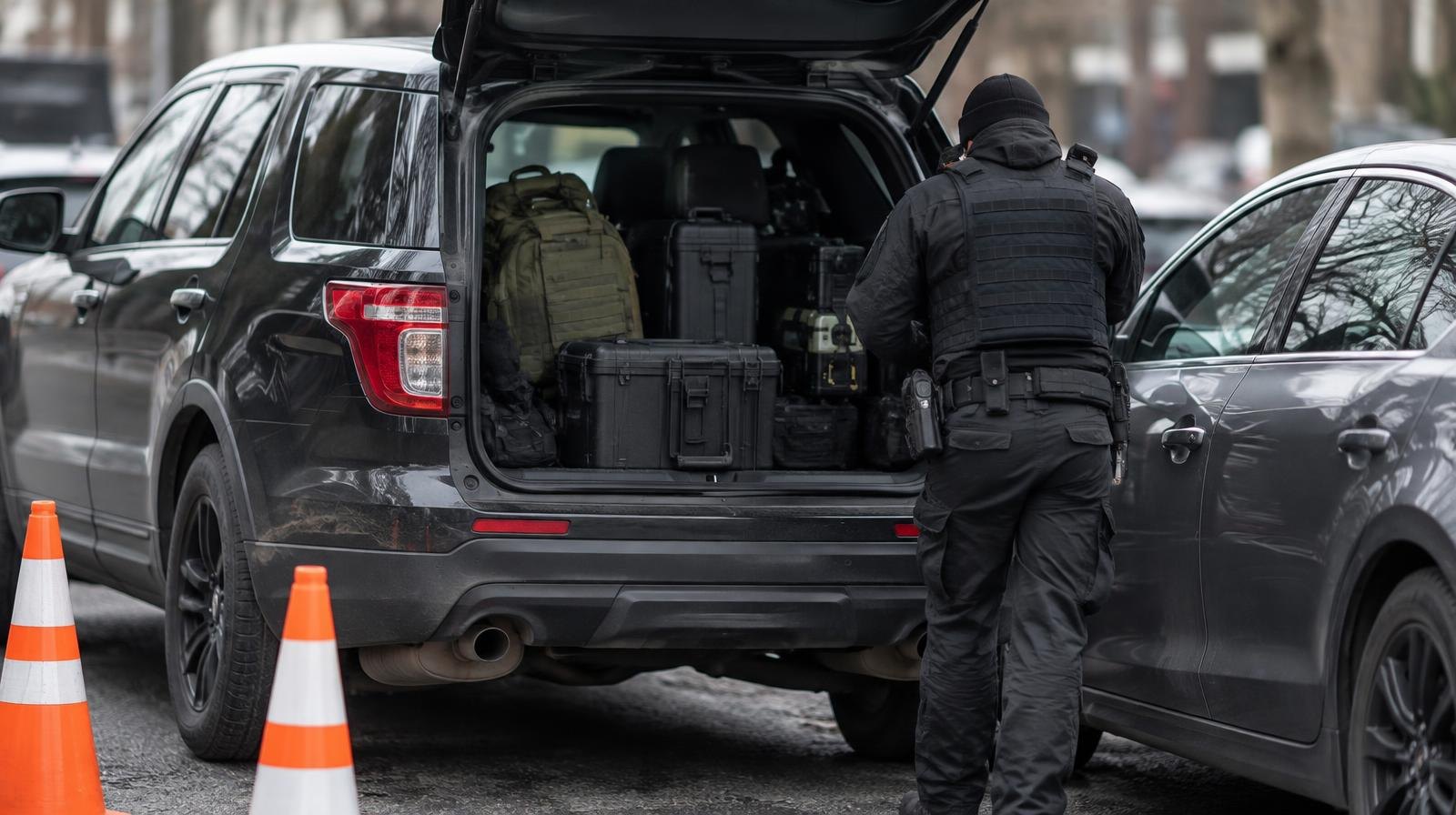 An unmarked dark SUV parked next to a sedan on a city street with traffic cones nearby.