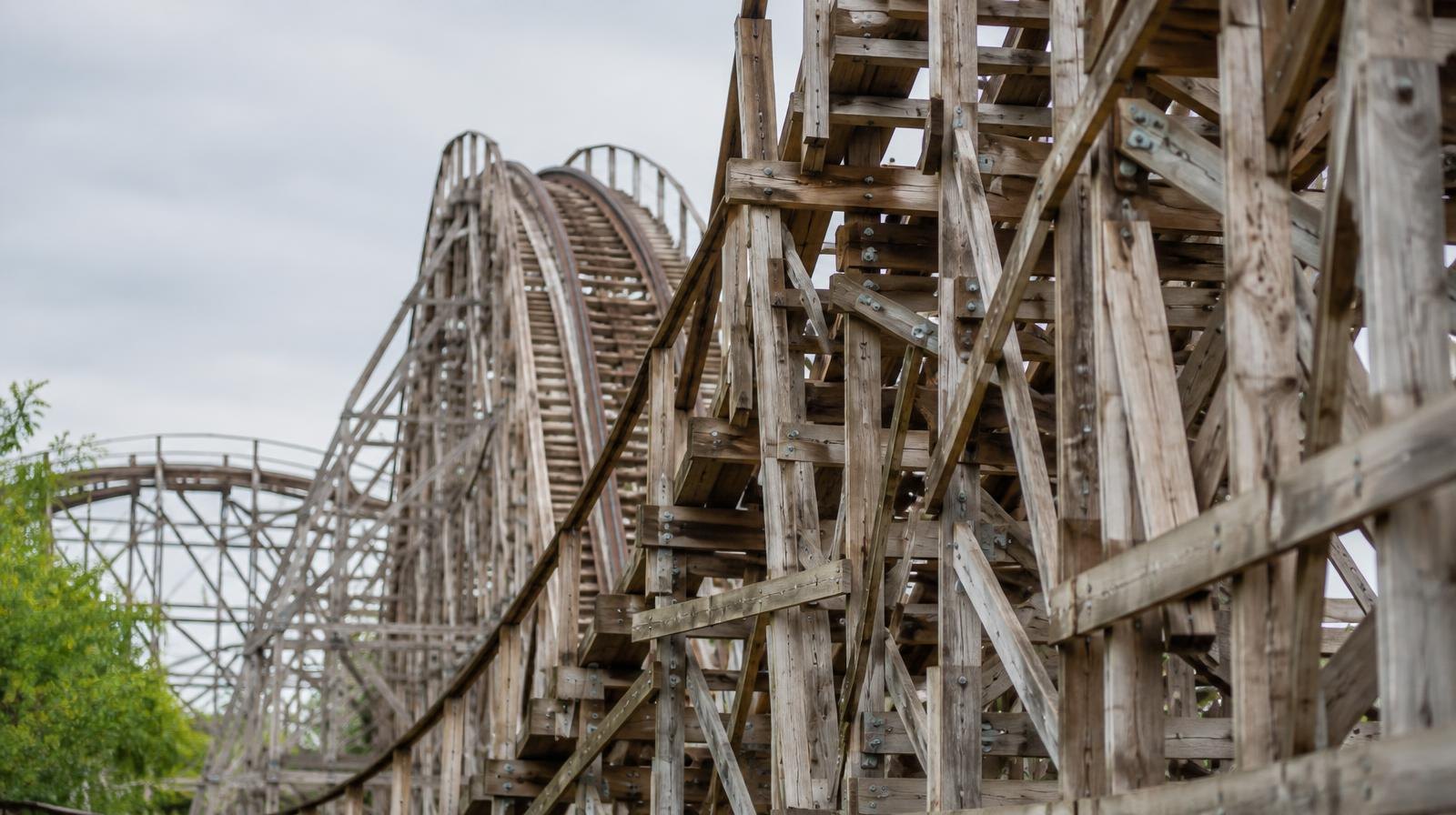 Wooden roller coaster timber lattice framework viewed from ground level under an overcast sky.