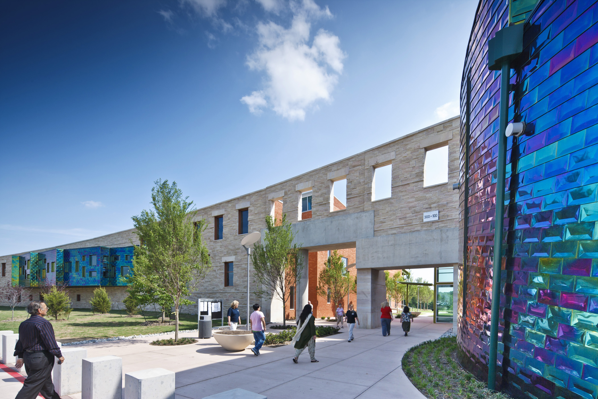 Exterior of a modern municipal complex with curved iridescent brick wall and limestone arched facade.