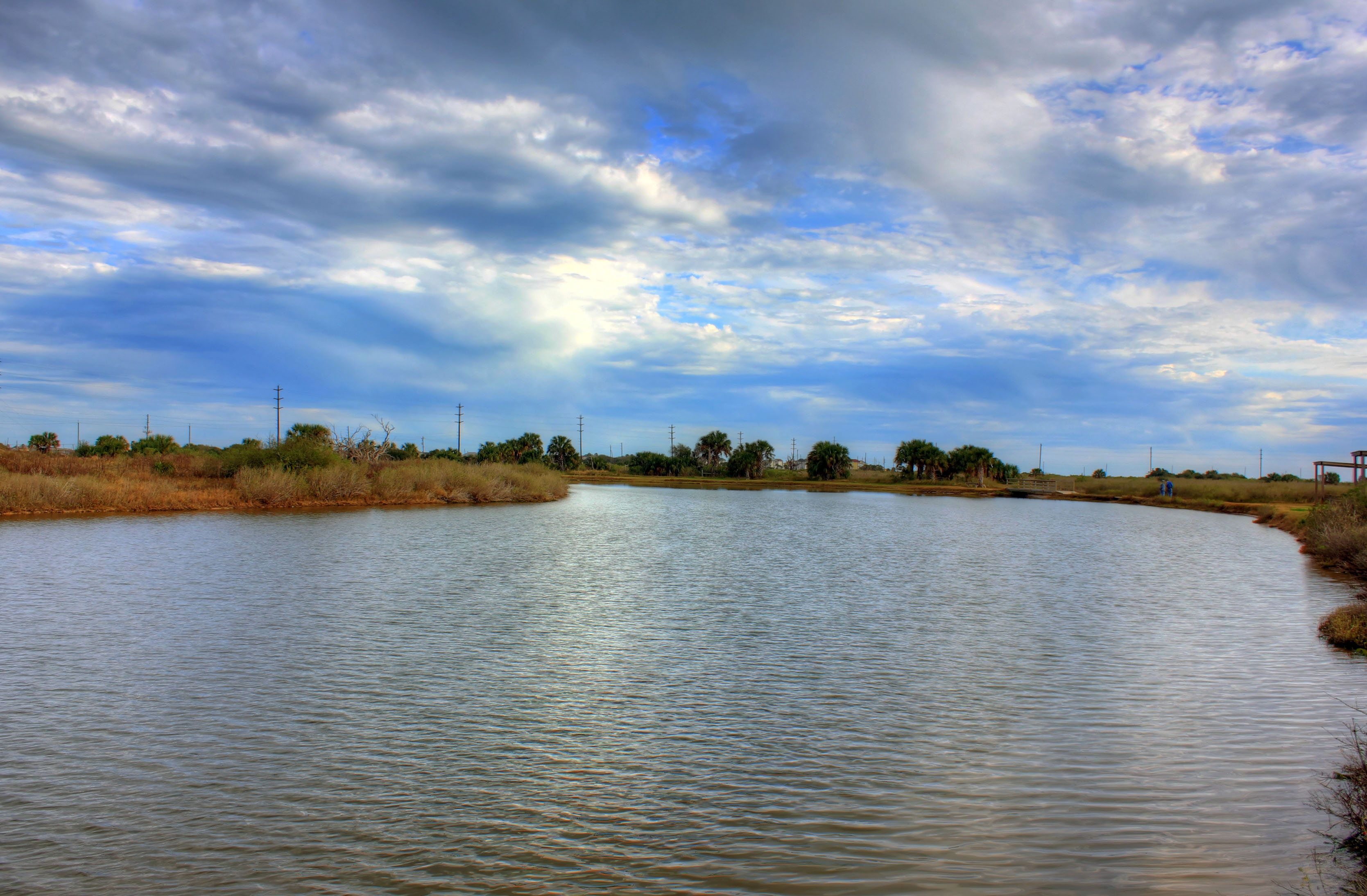 A calm estuary waterway curves through dry coastal grasses under a partly cloudy sky.