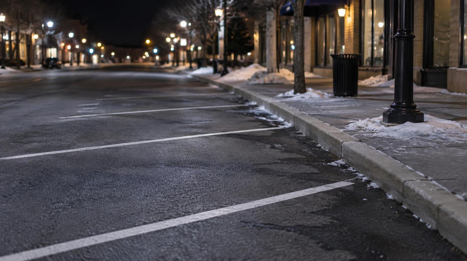 Empty angled parking spaces marked with white lines on a dark street under streetlights.