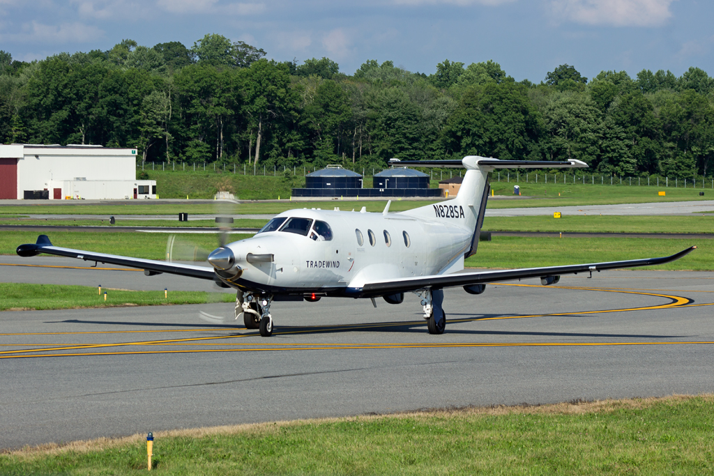 A white turboprop aircraft taxiing at Westchester County Airport with trees in the background.