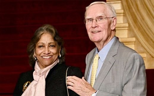 A smiling man and woman pose together in a formal indoor venue.