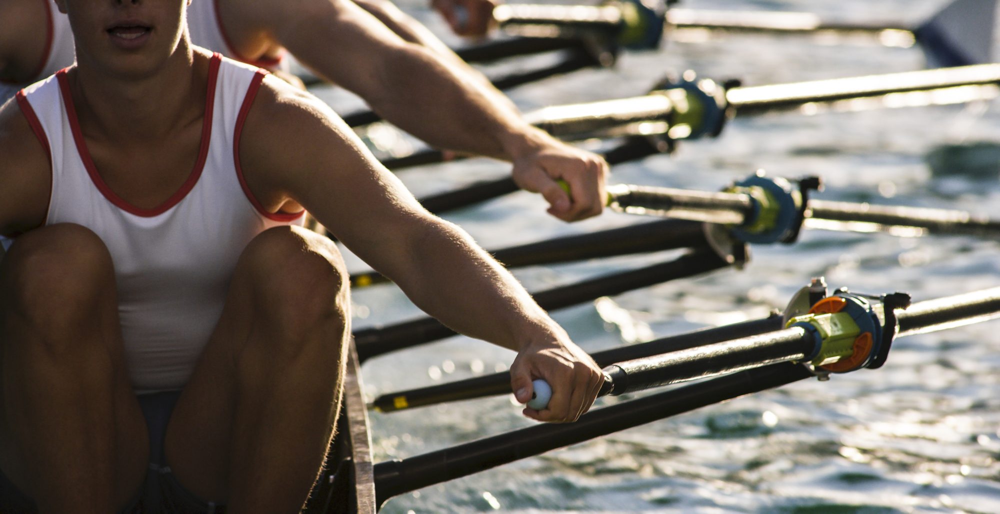 Close-up of rowers' arms and oars mid-stroke on the water during a race.