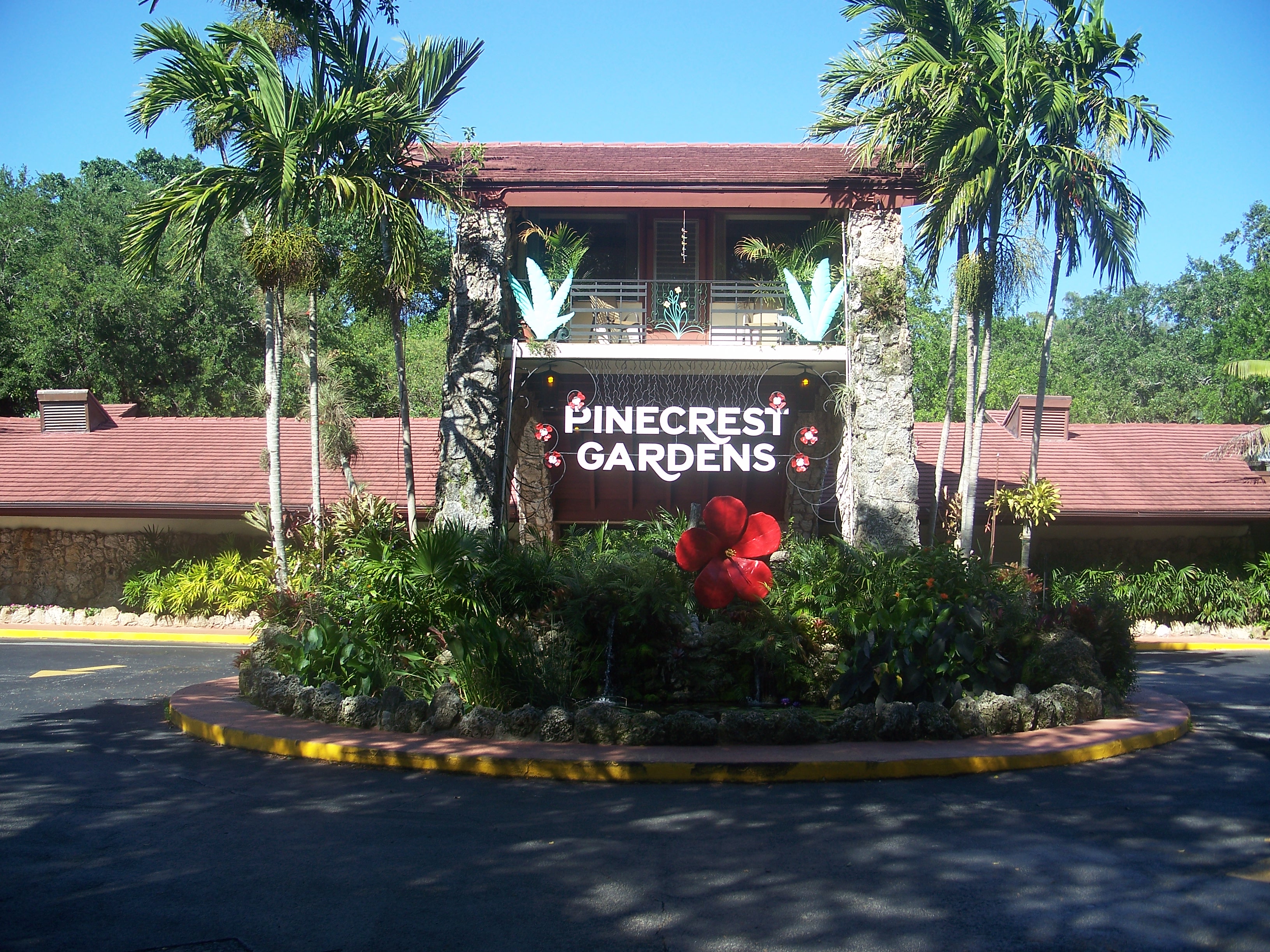 Entrance sign for Pinecrest Gardens surrounded by palm trees and tropical plants.