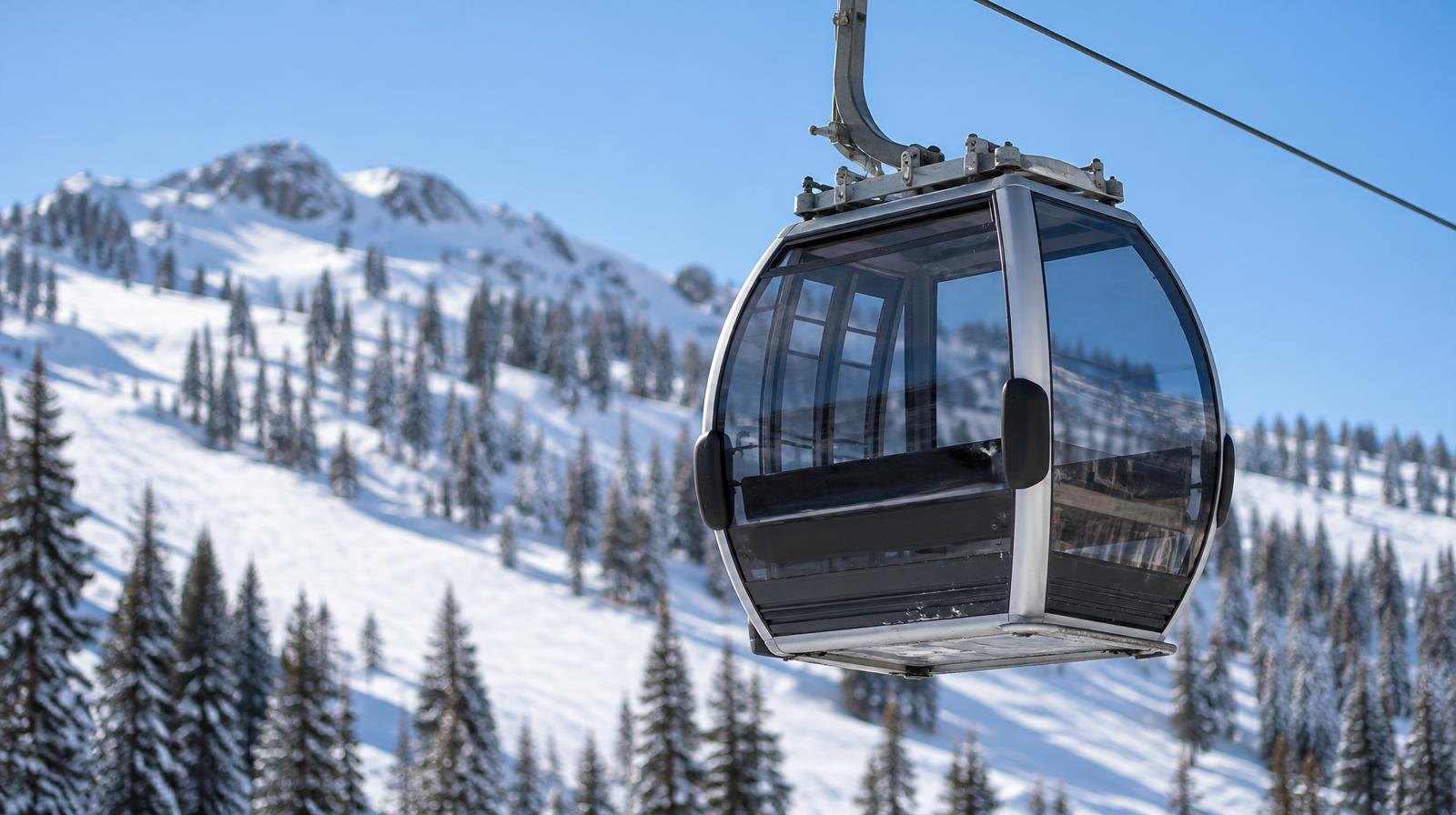 Enclosed gondola cabin suspended on a cable above a snowy mountain slope.