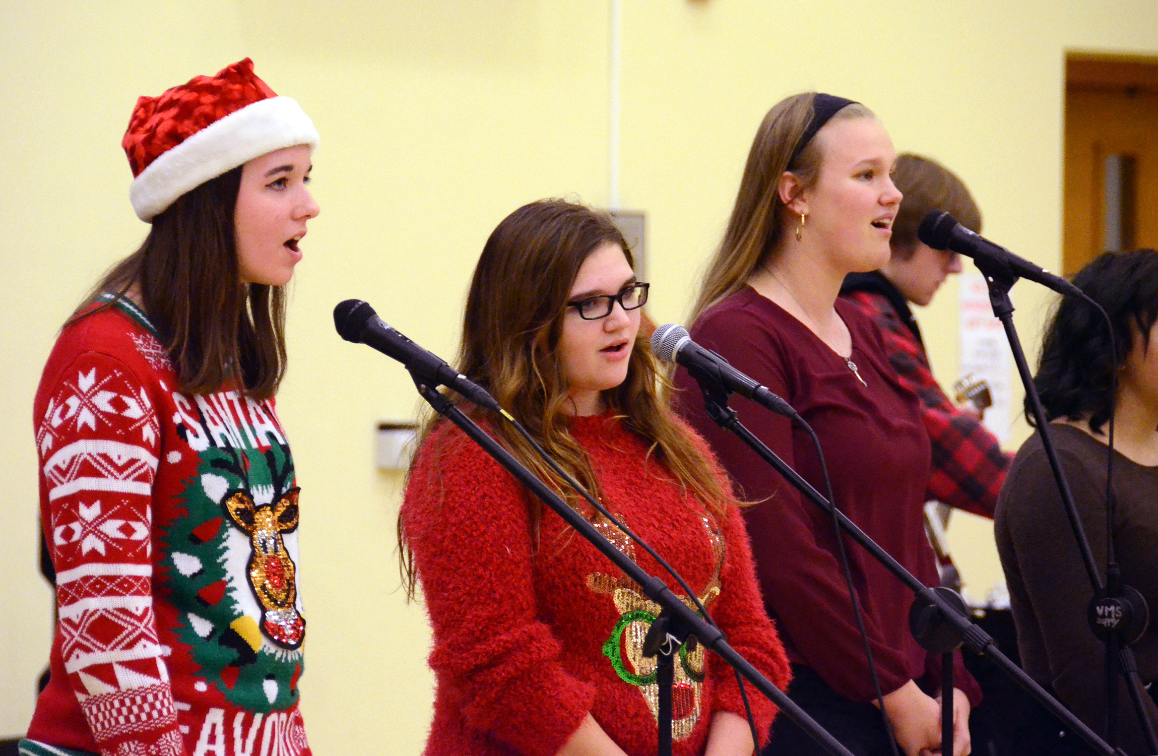 Three young women singing into microphones at a school holiday concert.