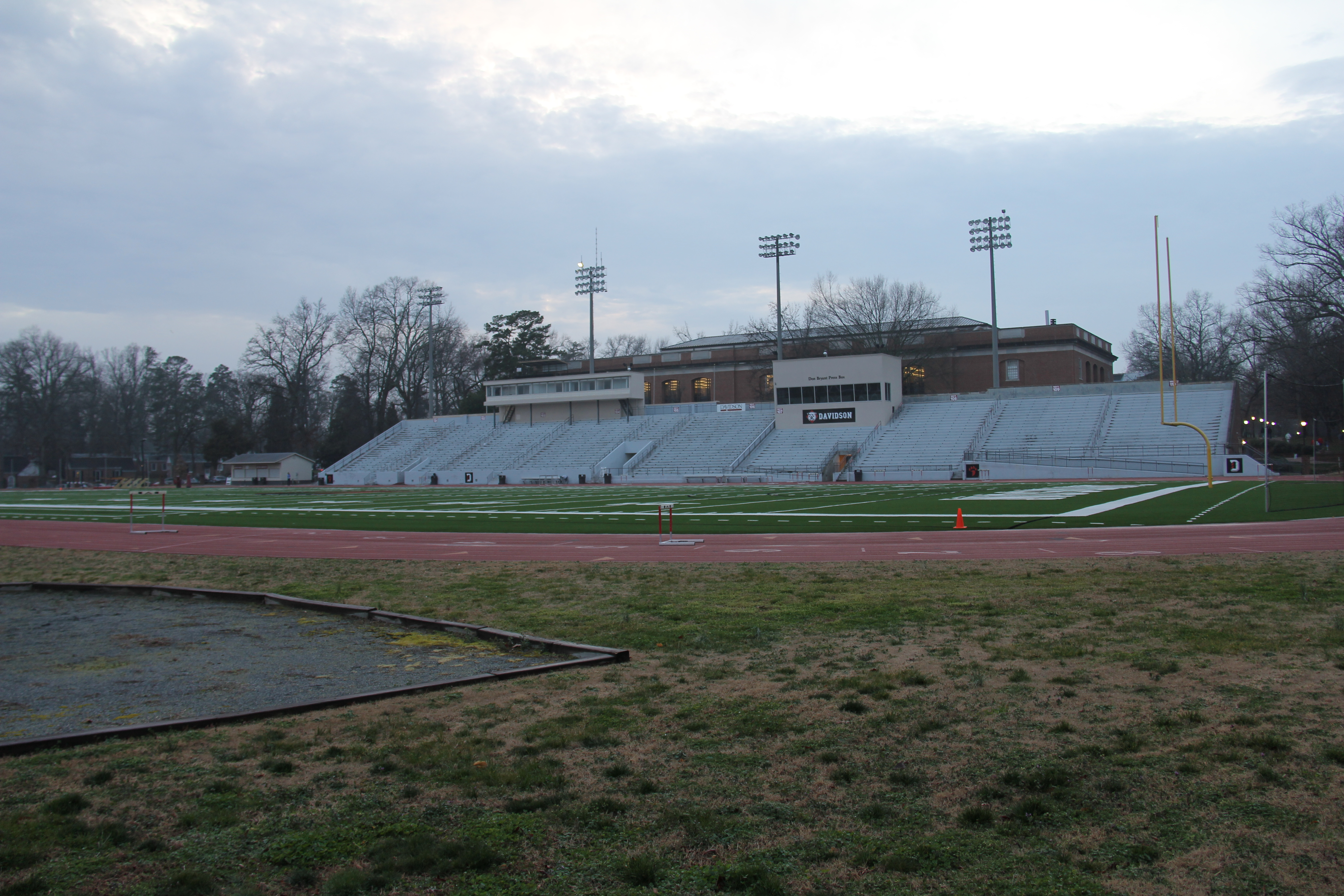 Empty football stadium with white concrete bleachers, light towers, and a grass field.