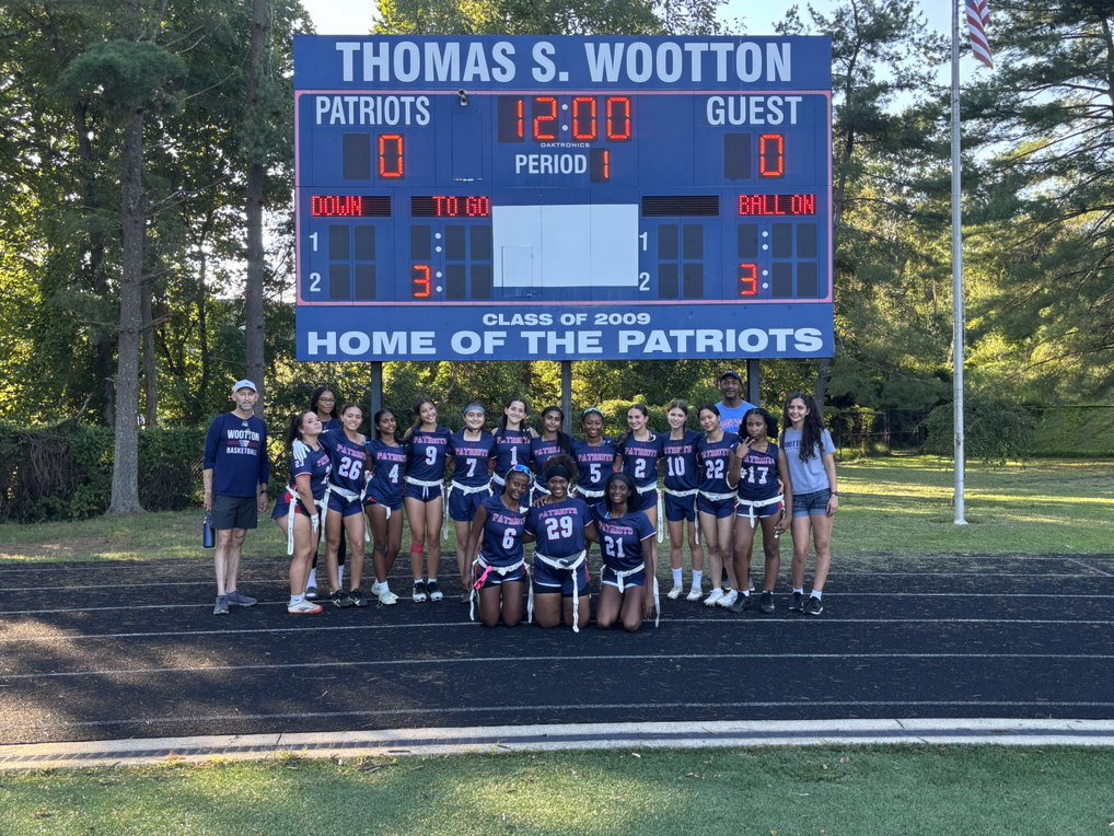 A group of female athletes in navy uniforms pose in front of a high school scoreboard.