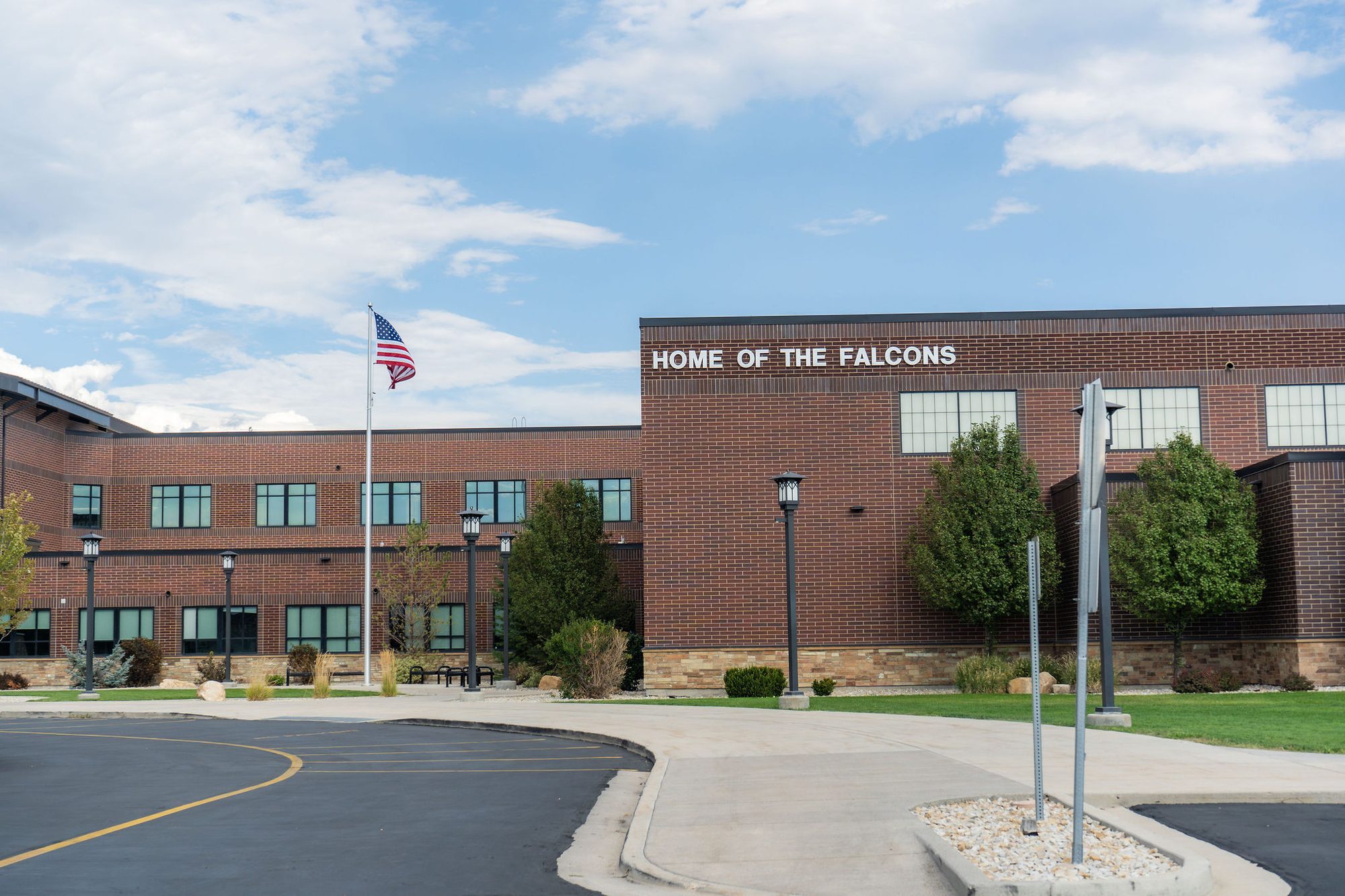 Brick high school building exterior with flagpole and Home of the Falcons sign.