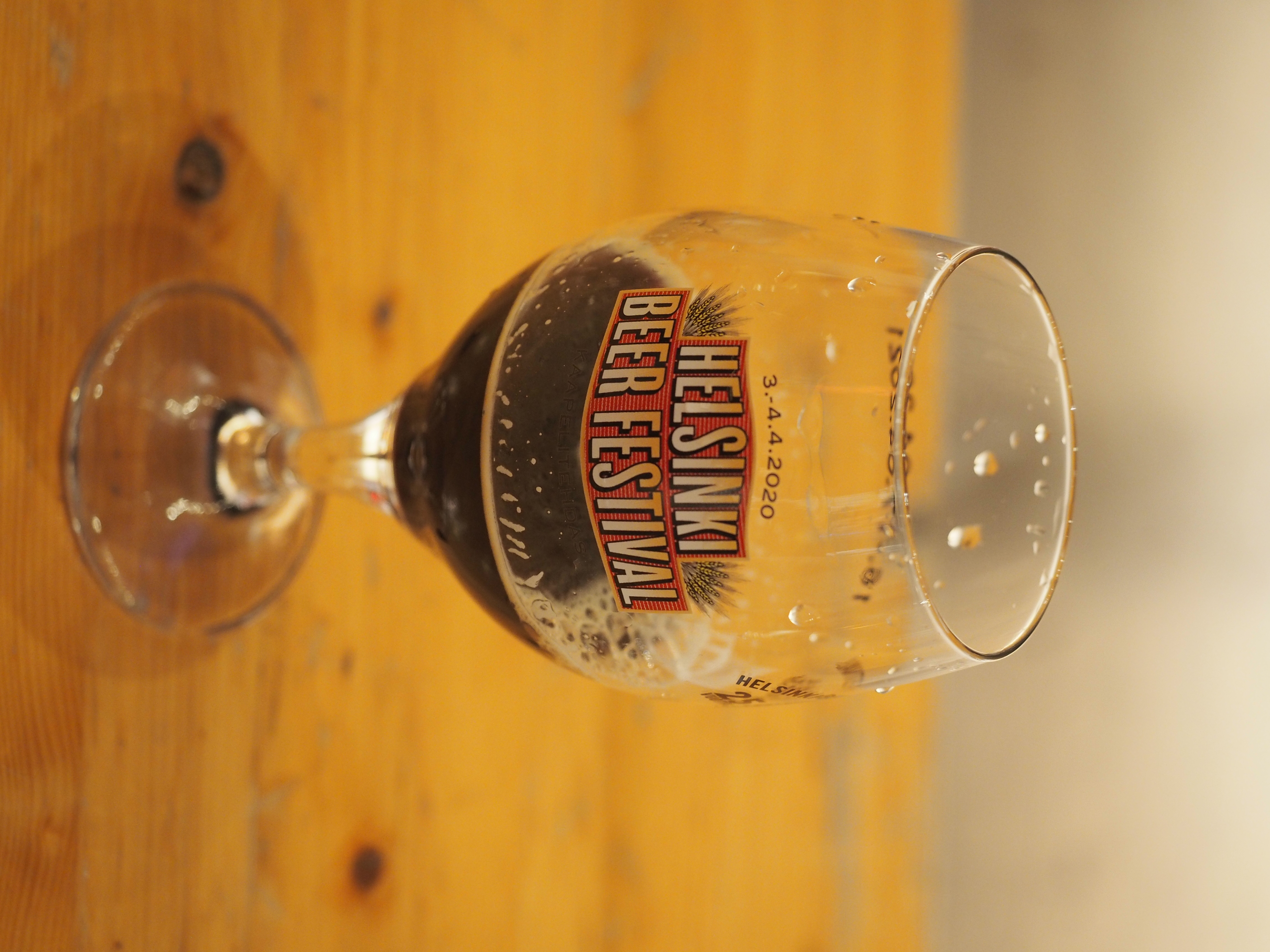A stemmed tulip glass holding a small pour of dark beer on a wooden table.