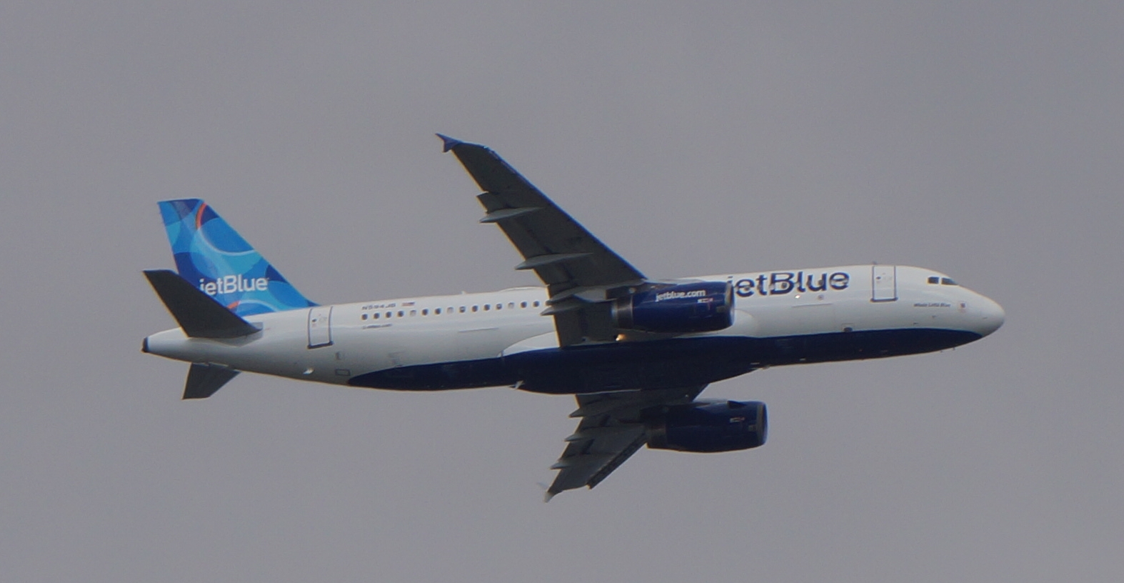 A JetBlue passenger jet in flight against an overcast sky.