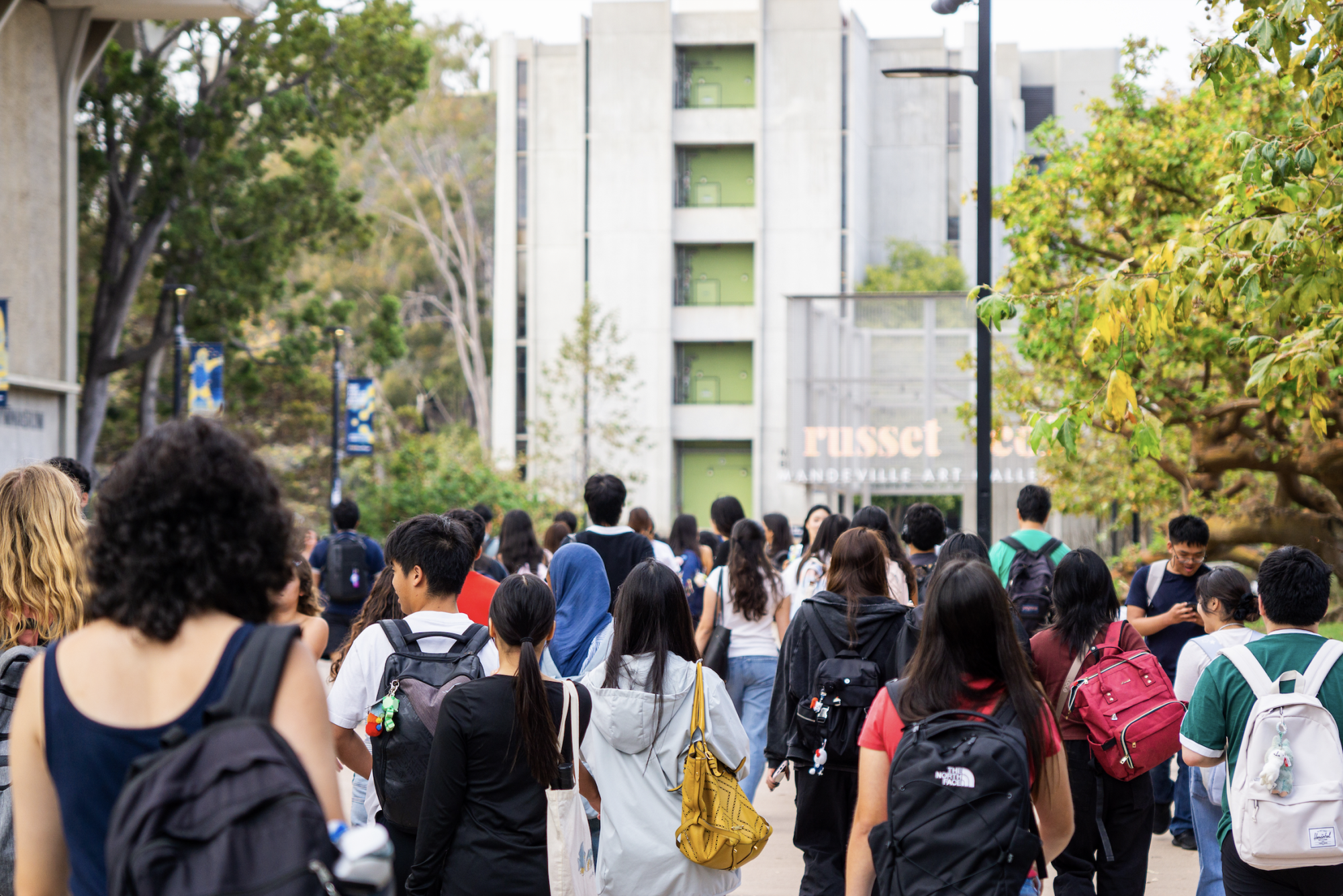 Students with backpacks walking along an outdoor university campus pathway.
