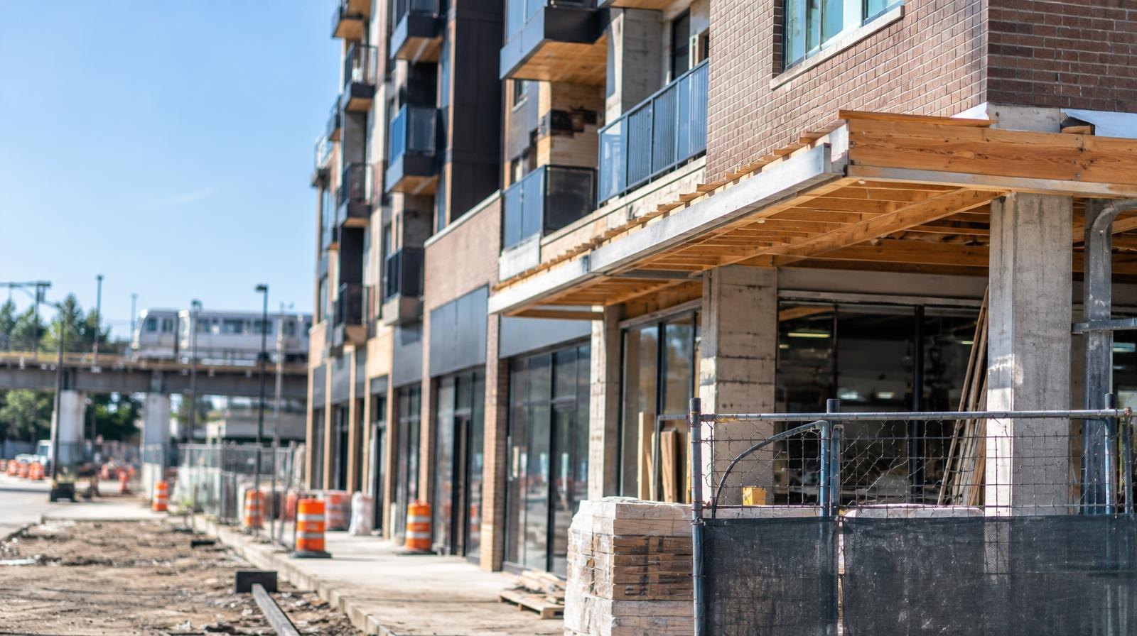 A modern mid-rise apartment building with ground-floor retail storefronts under a clear sky.