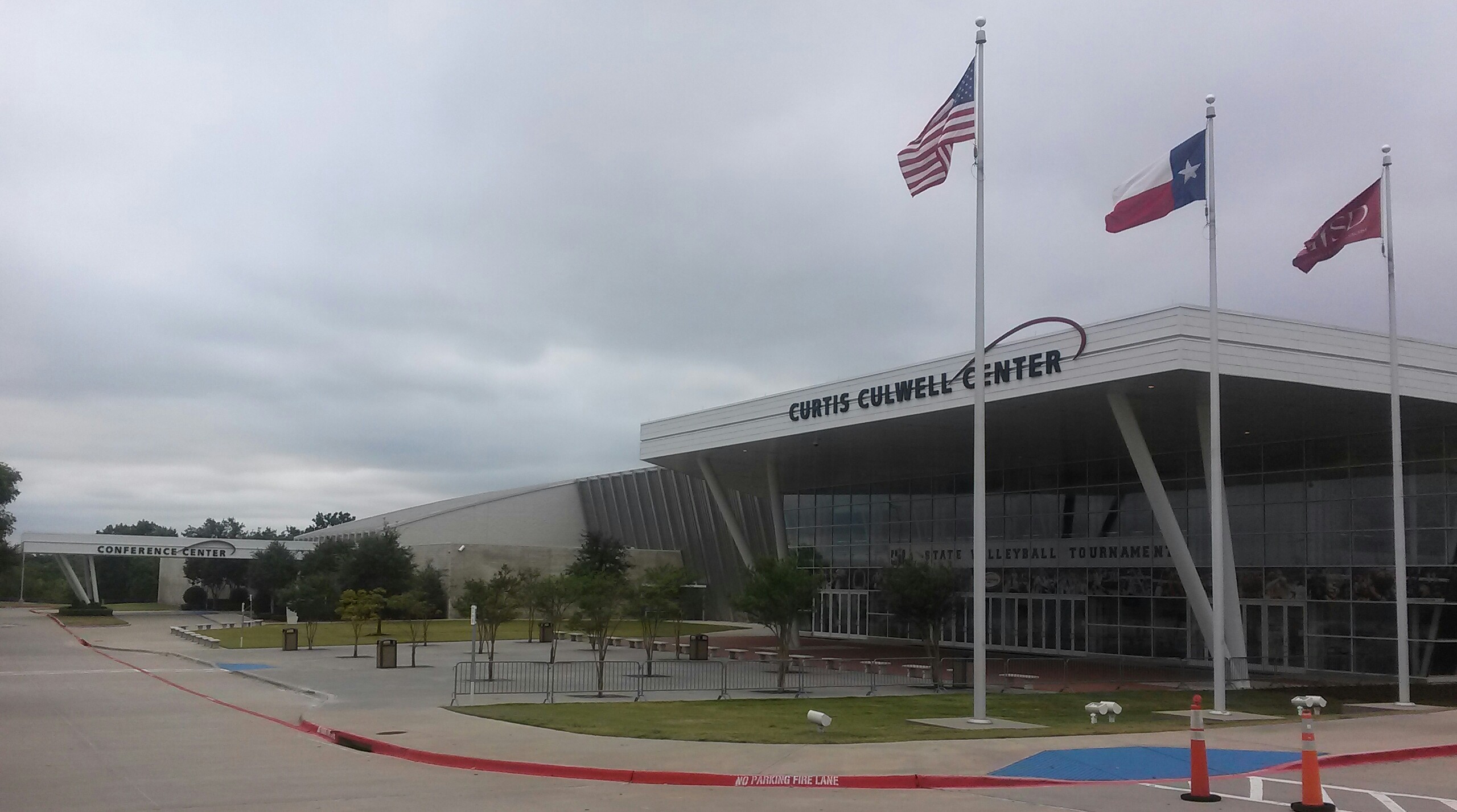 Exterior of a large modern building with three flagpoles flying U.S. and Texas flags.