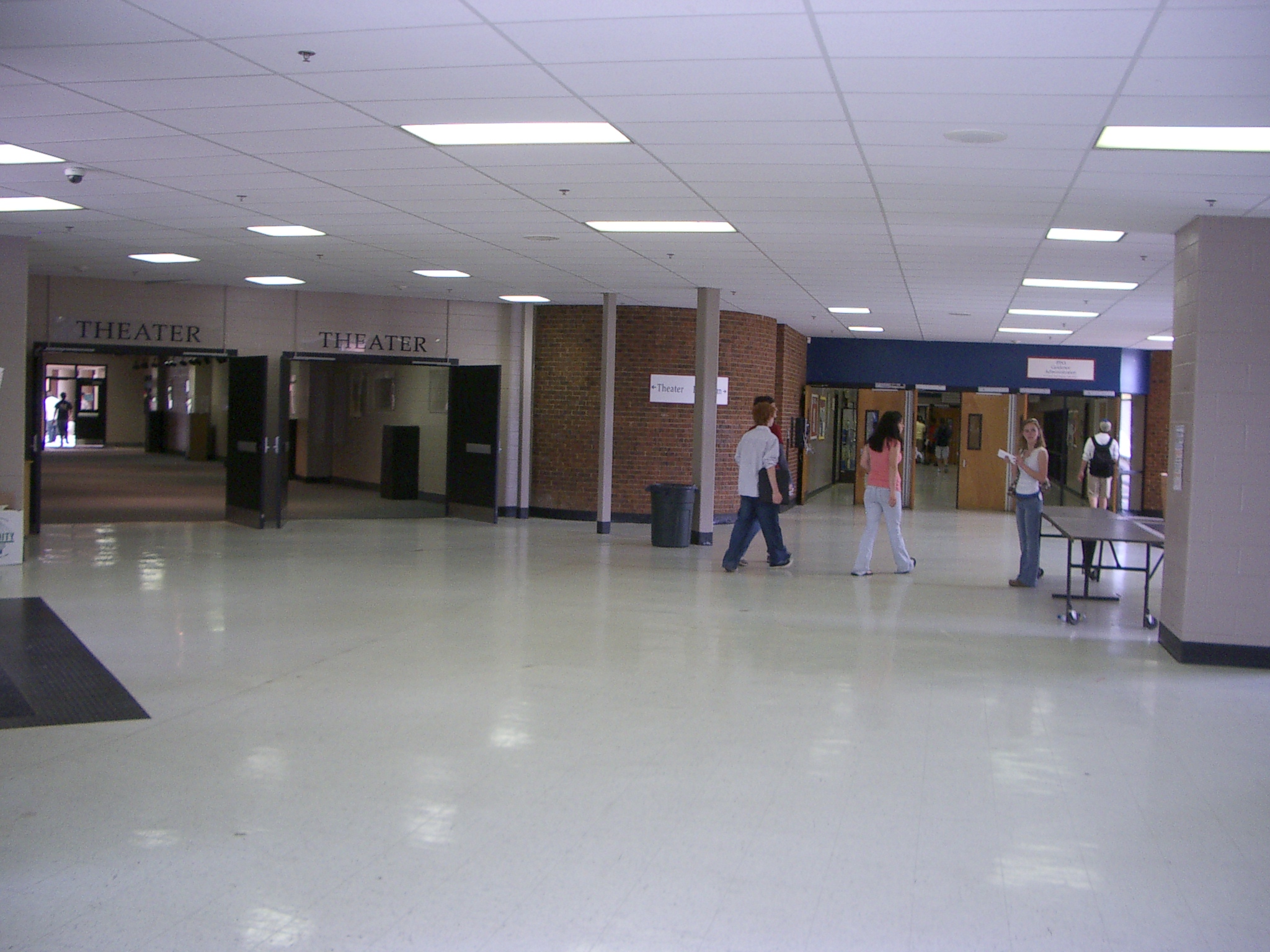 Wide school hallway with tiled floor, brick columns, and theater signage.