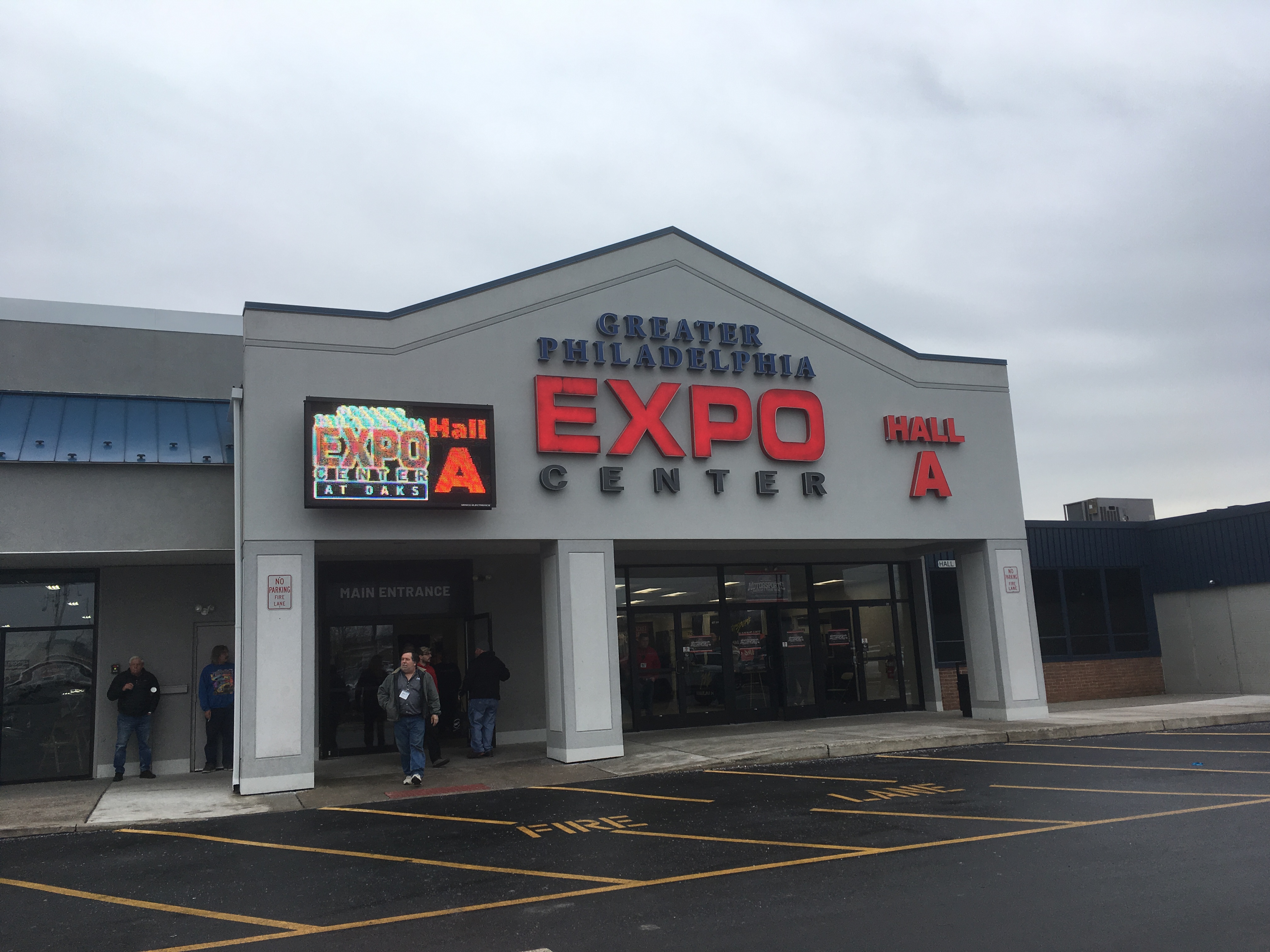 Exterior entrance of a large expo center building with glass doors and overhead signage.