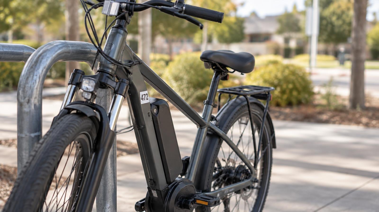 Electric bicycle leaning against a metal bike rack on a paved path.
