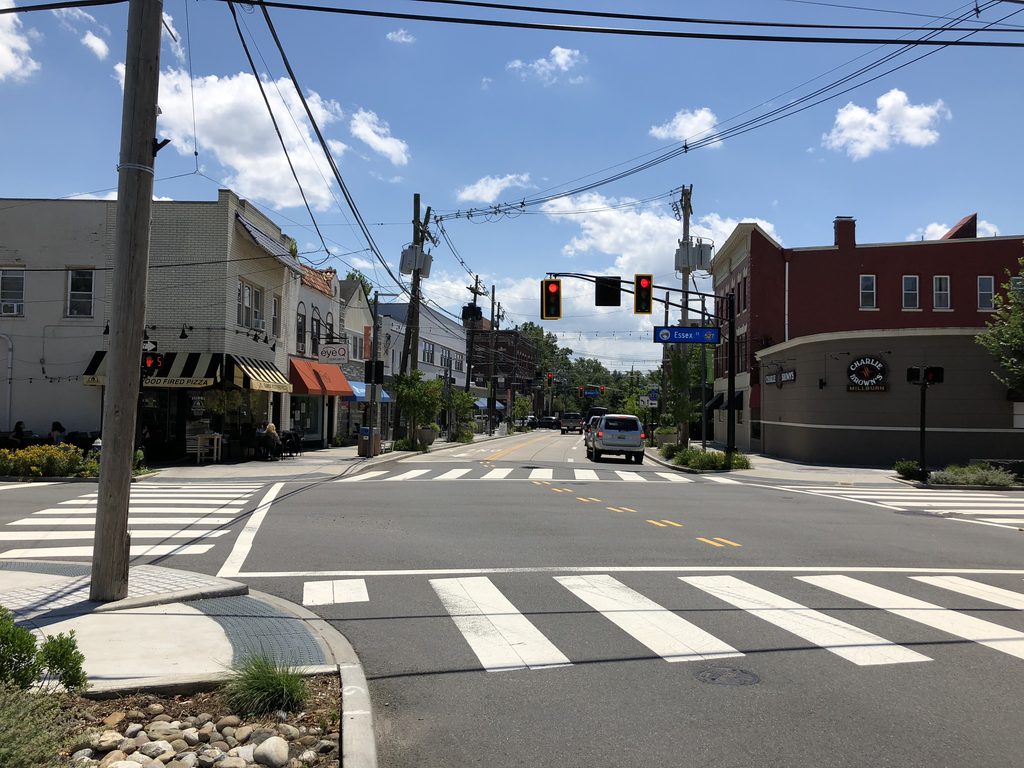 Downtown intersection with storefronts, traffic signals, and tree-lined streets in Millburn, New Jersey.