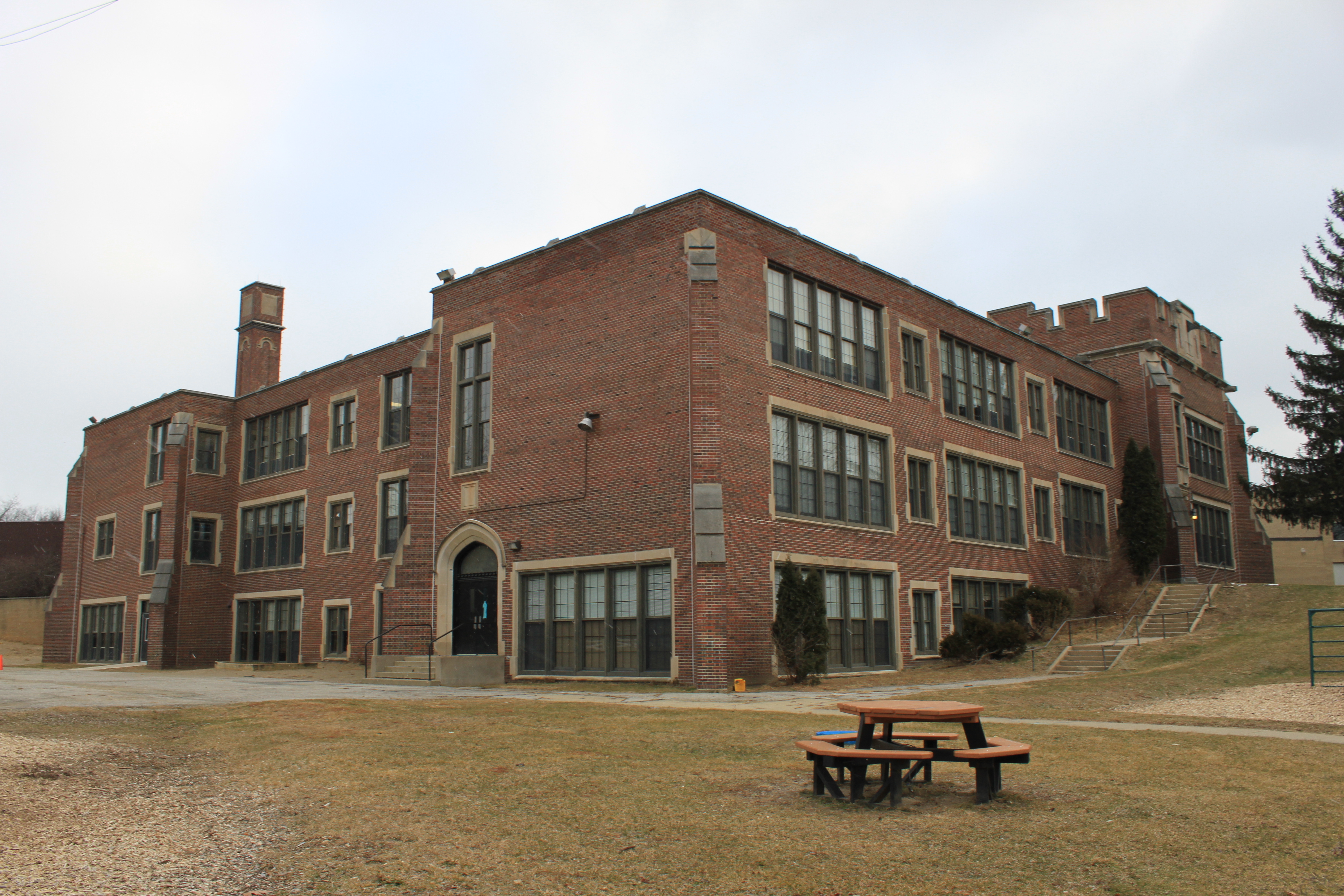 Three-story red brick school building with a picnic table on a grassy lawn.