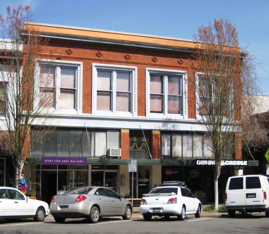Historic two-story brick building with storefronts along a downtown Salem street with parked cars.