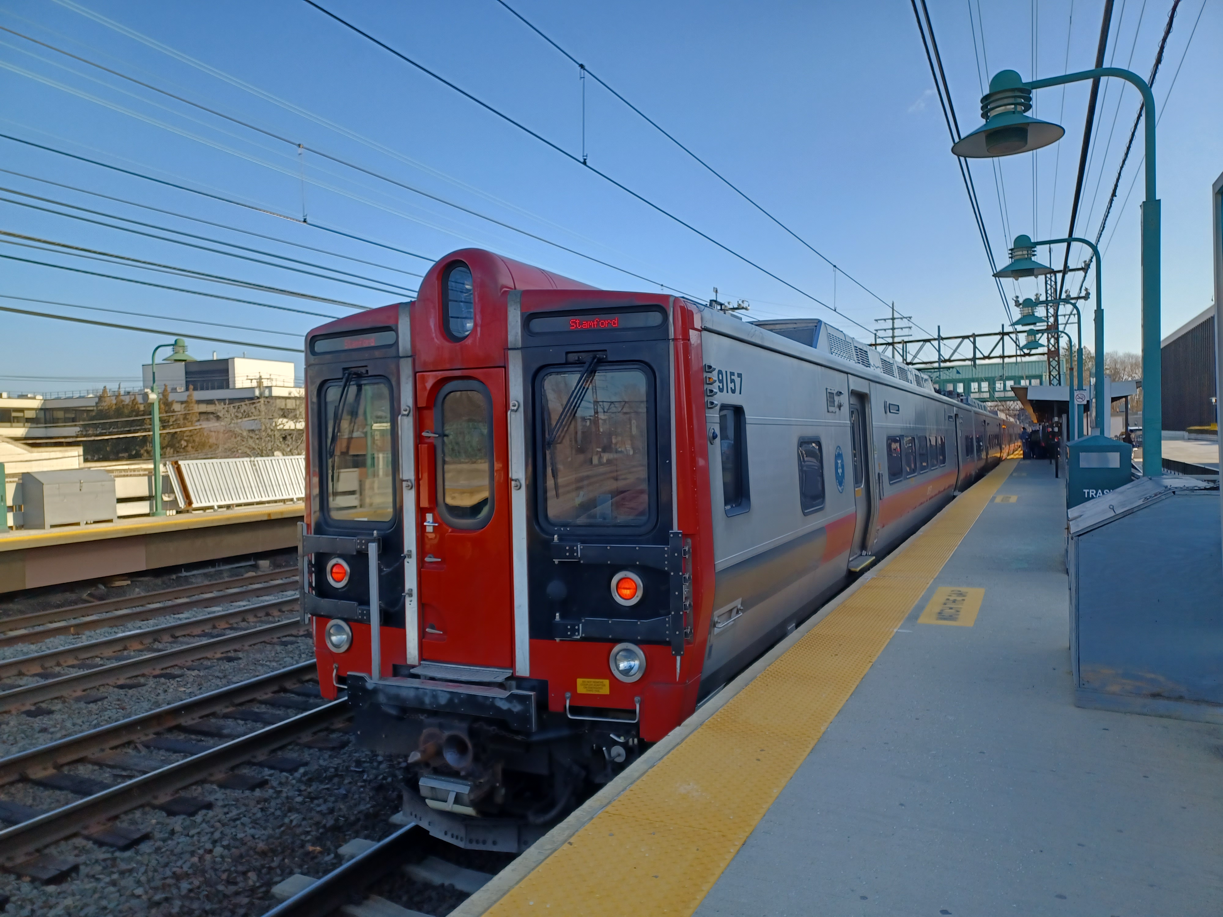 Red and silver Metro-North commuter train stopped at a station platform with overhead catenary wires.