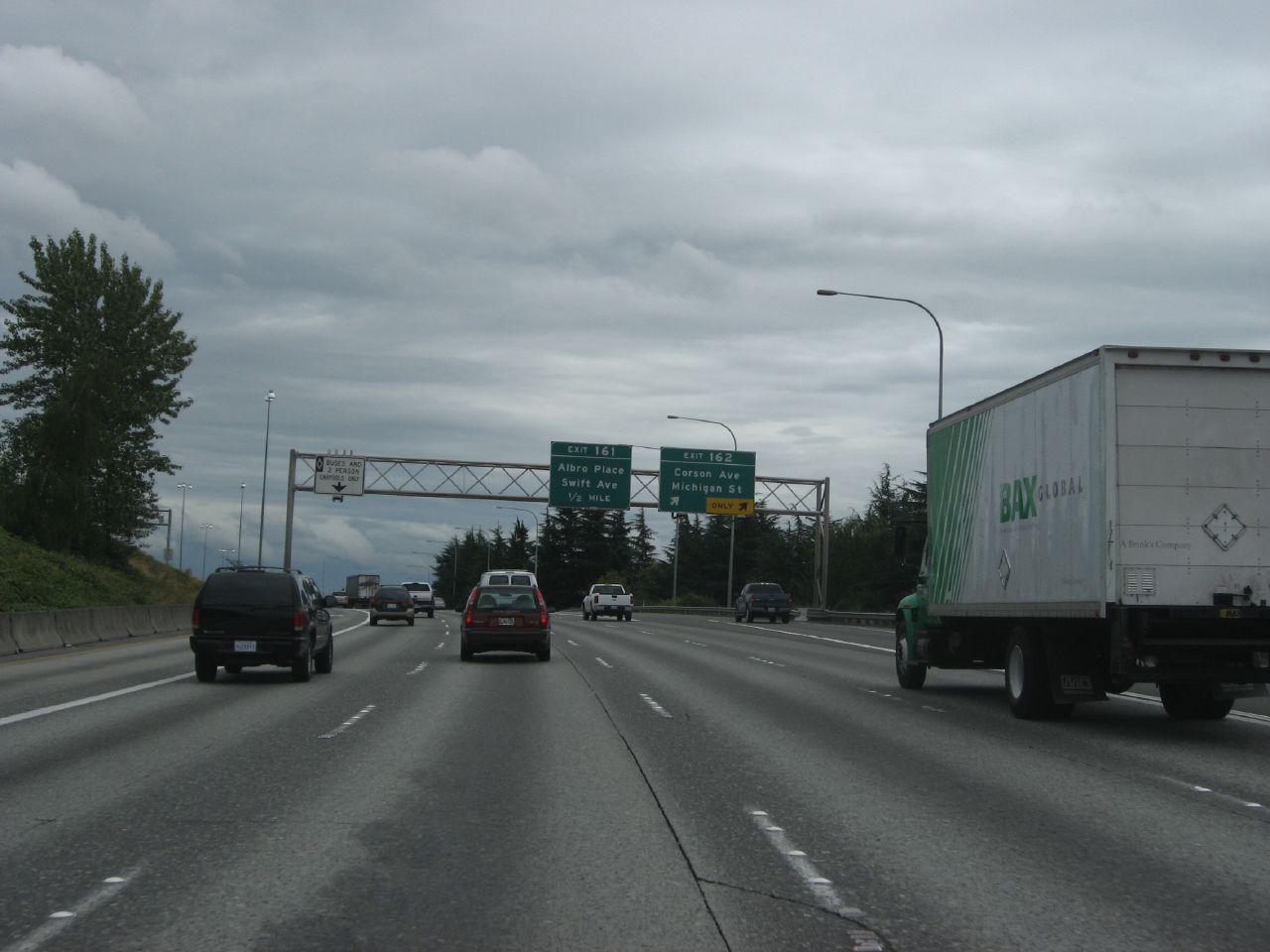 Multi-lane interstate highway with overhead green directional signs and traffic under overcast skies.