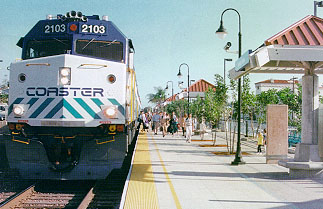 A blue COASTER commuter train stopped at a station platform with passengers waiting.