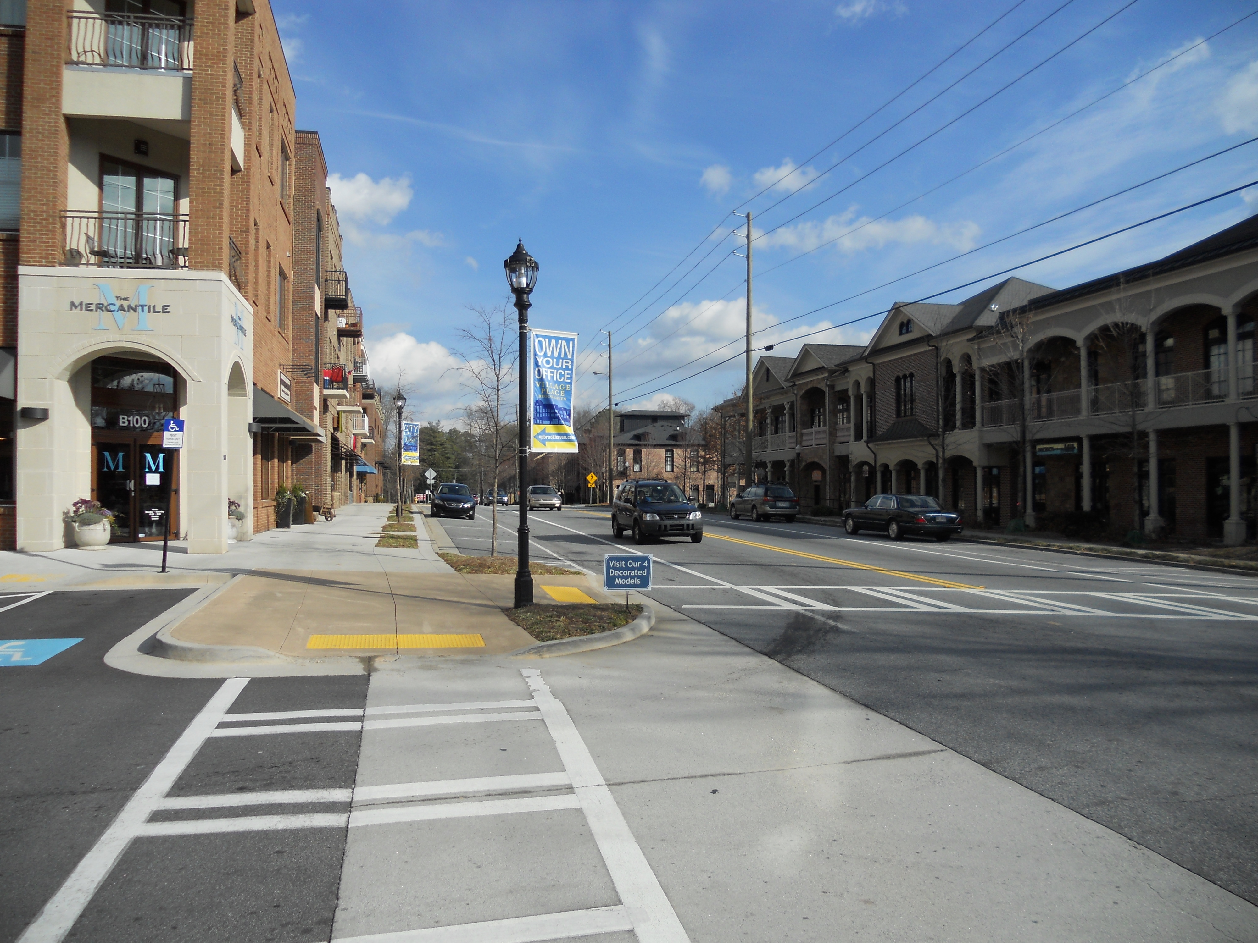 Brick mixed-use buildings and a decorative street lamp along a wide intersection in Brookhaven Village.