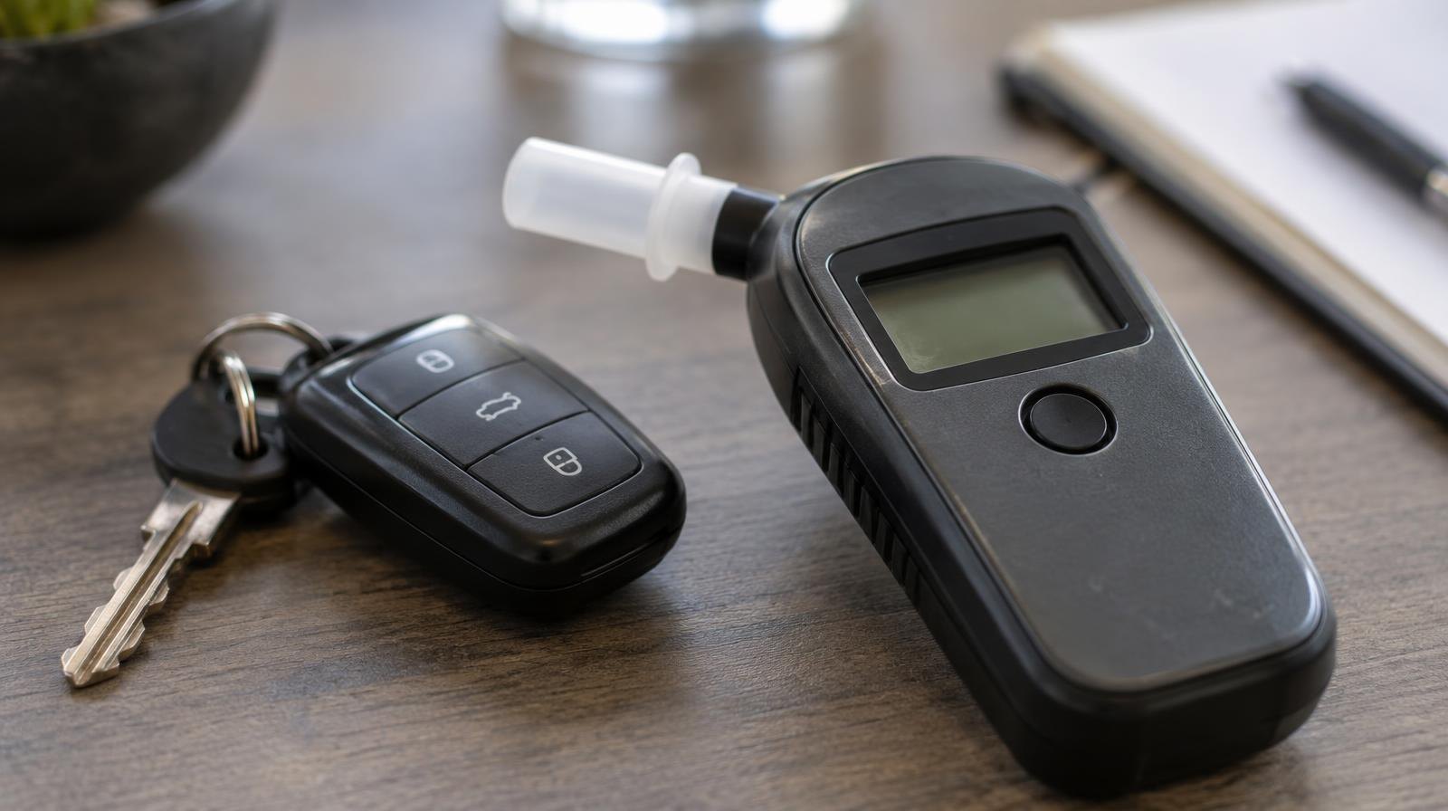 A breathalyzer device resting on a surface next to a set of car keys.