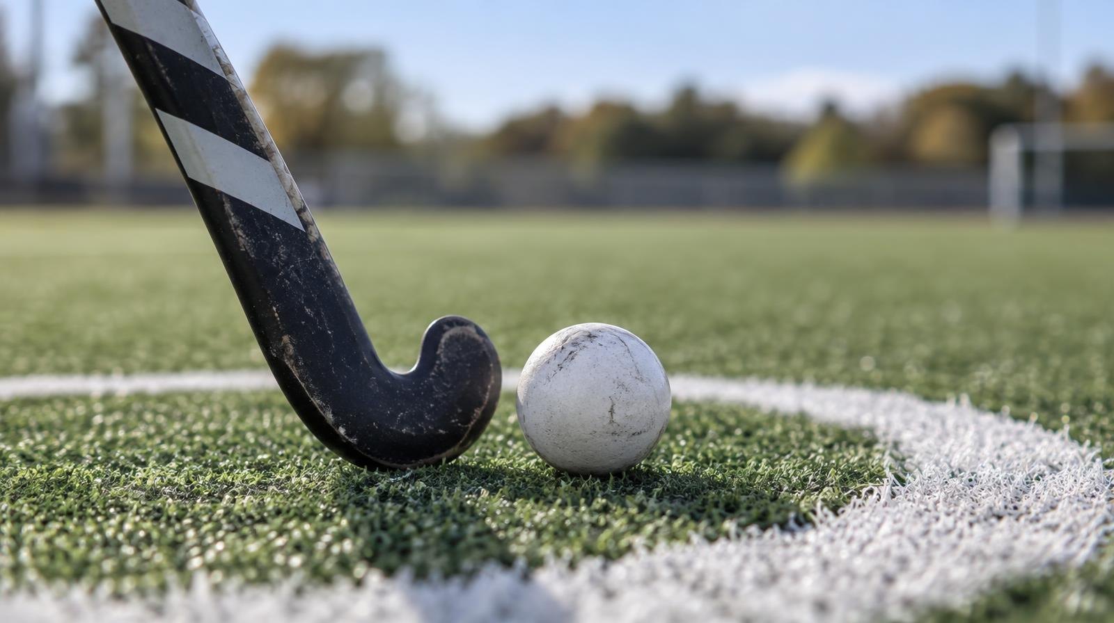 A field hockey stick and ball resting on green artificial turf near a white painted circle.