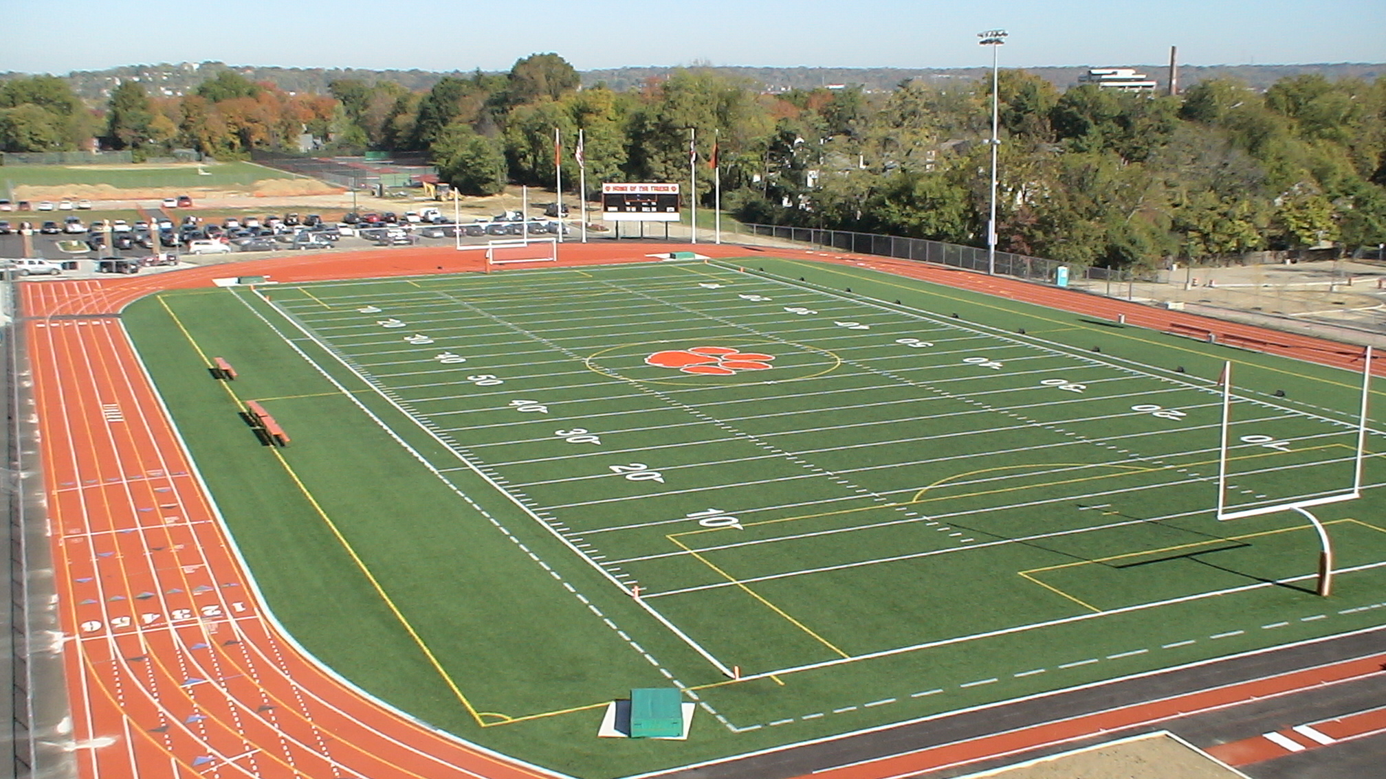 Aerial view of a high school football stadium with artificial turf and orange running track.