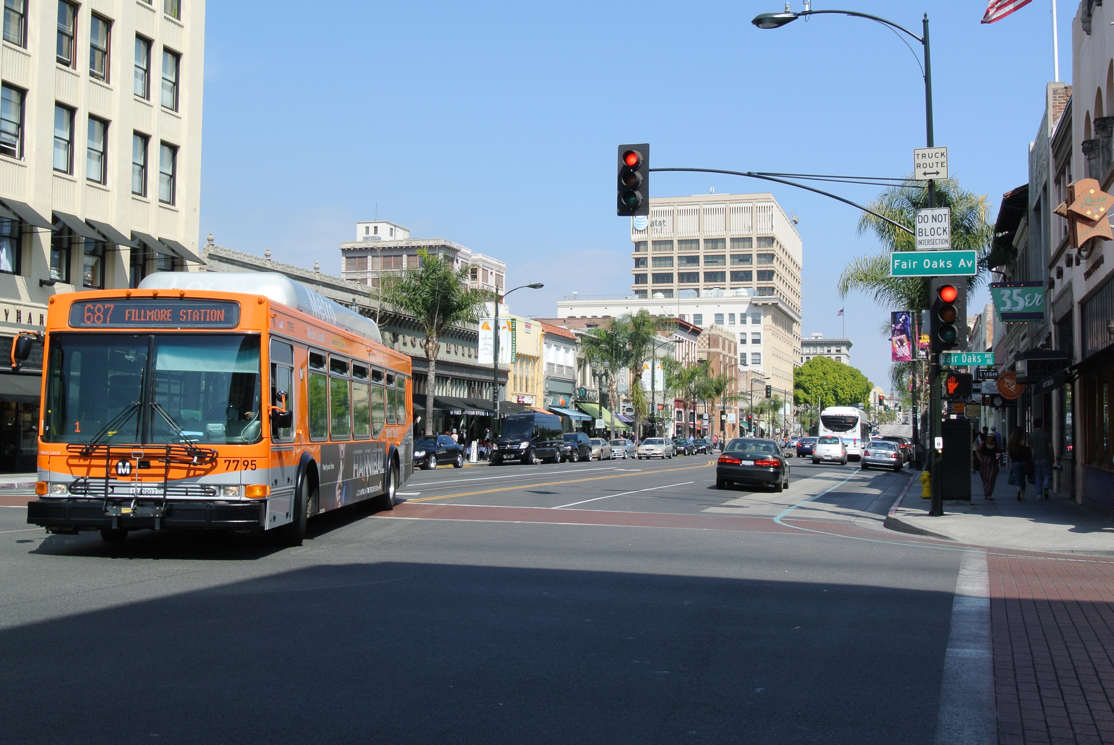 Busy street intersection with a bus, palm trees, and commercial buildings.
