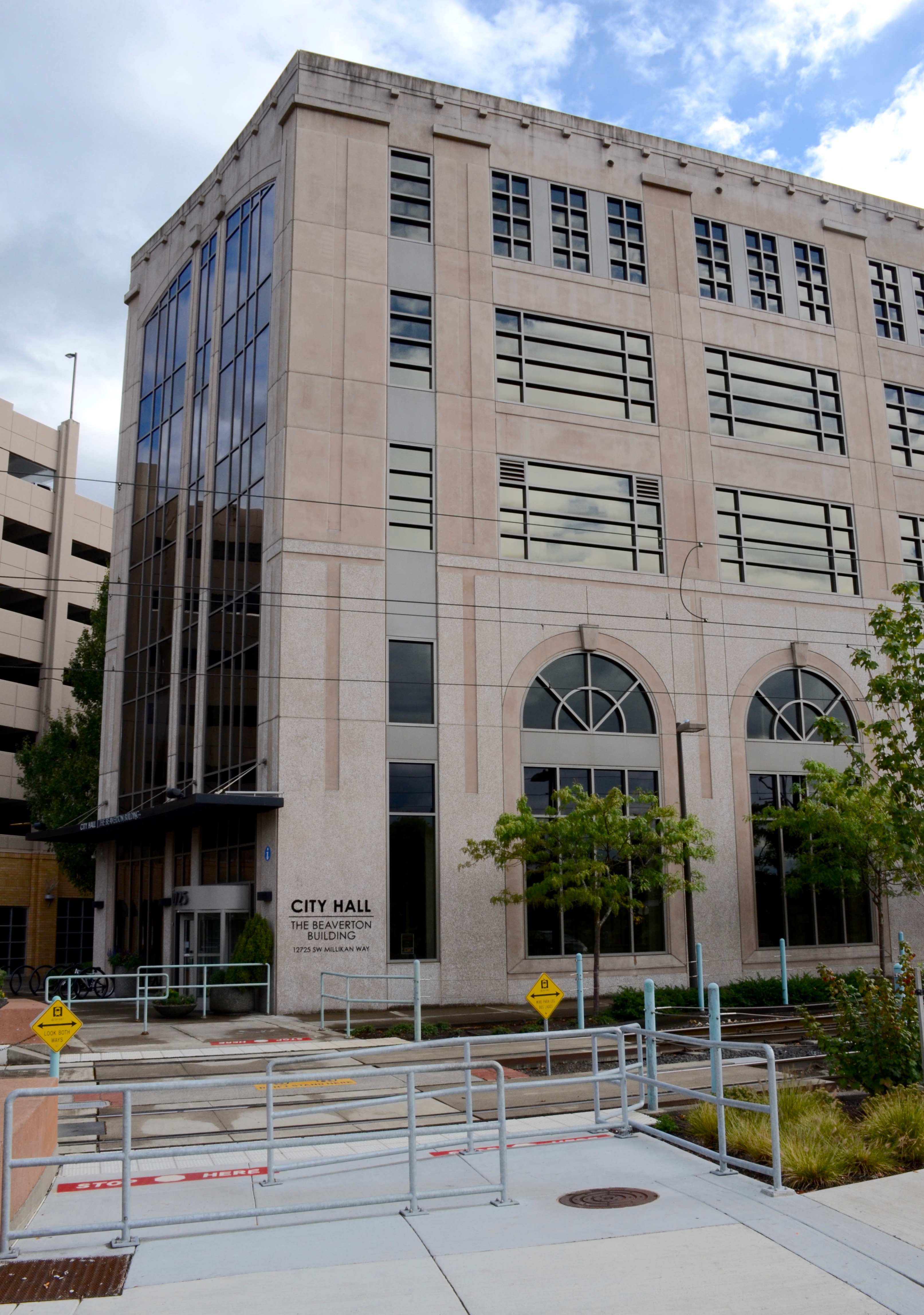 Multi-story beige City Hall building with MAX light rail tracks in the foreground.